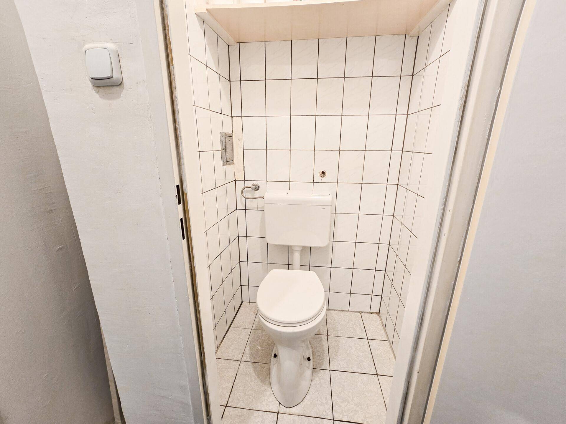 Separate Toilette mit weißen Fliesen und einfacher, funktionaler Ausstattung.