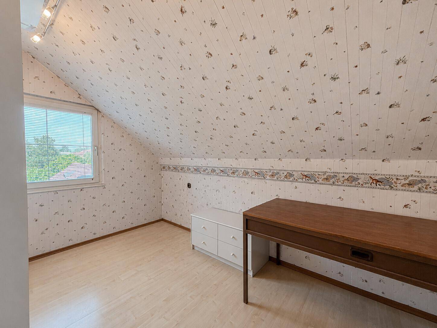 Dachzimmer mit hellem Laminatboden und Schreibtisch, ideal als Arbeitszimmer.