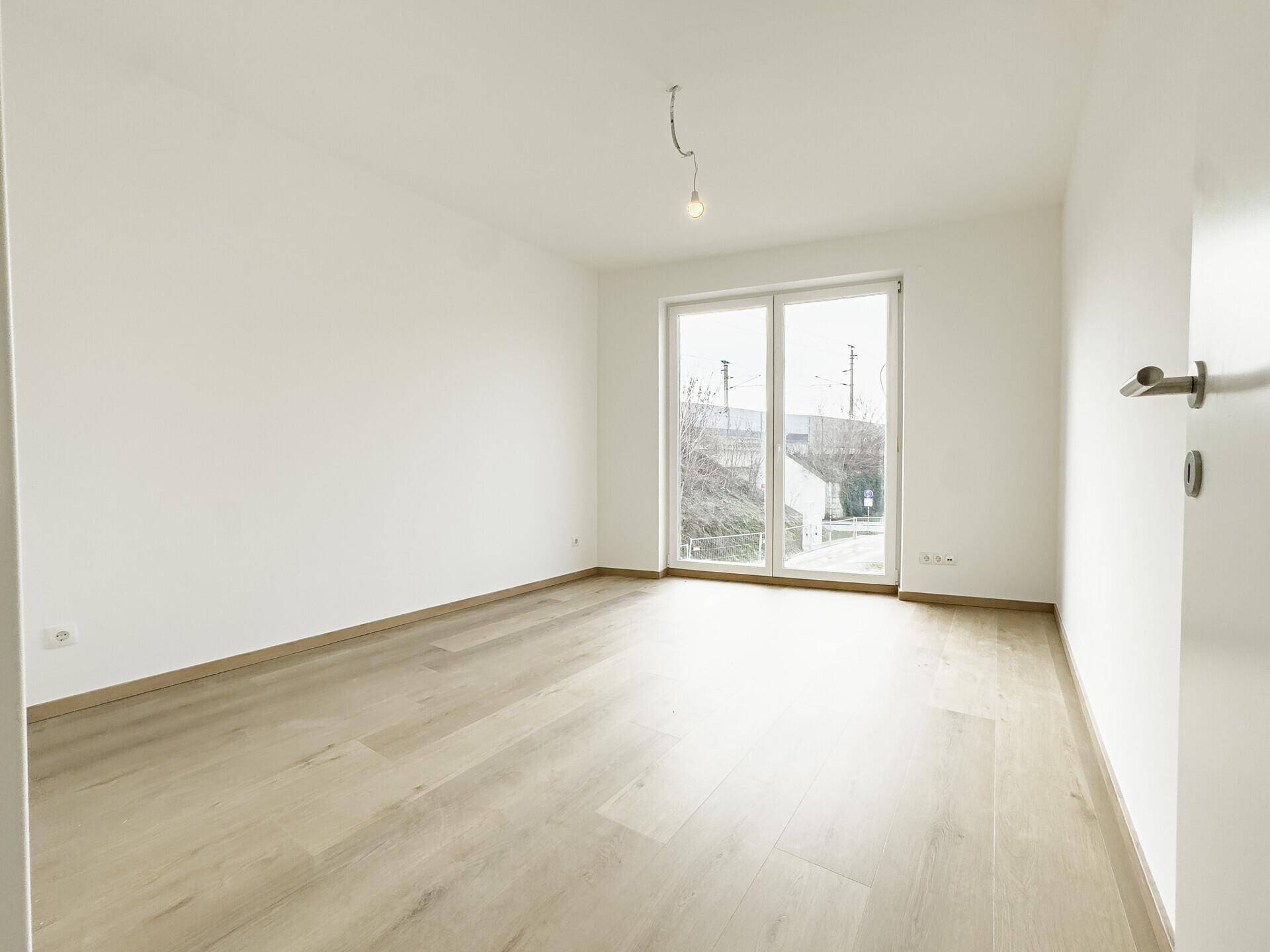 Geräumiges Schlafzimmer mit hellem Holzboden und großem Fenster, das viel Tageslicht hereinlässt.