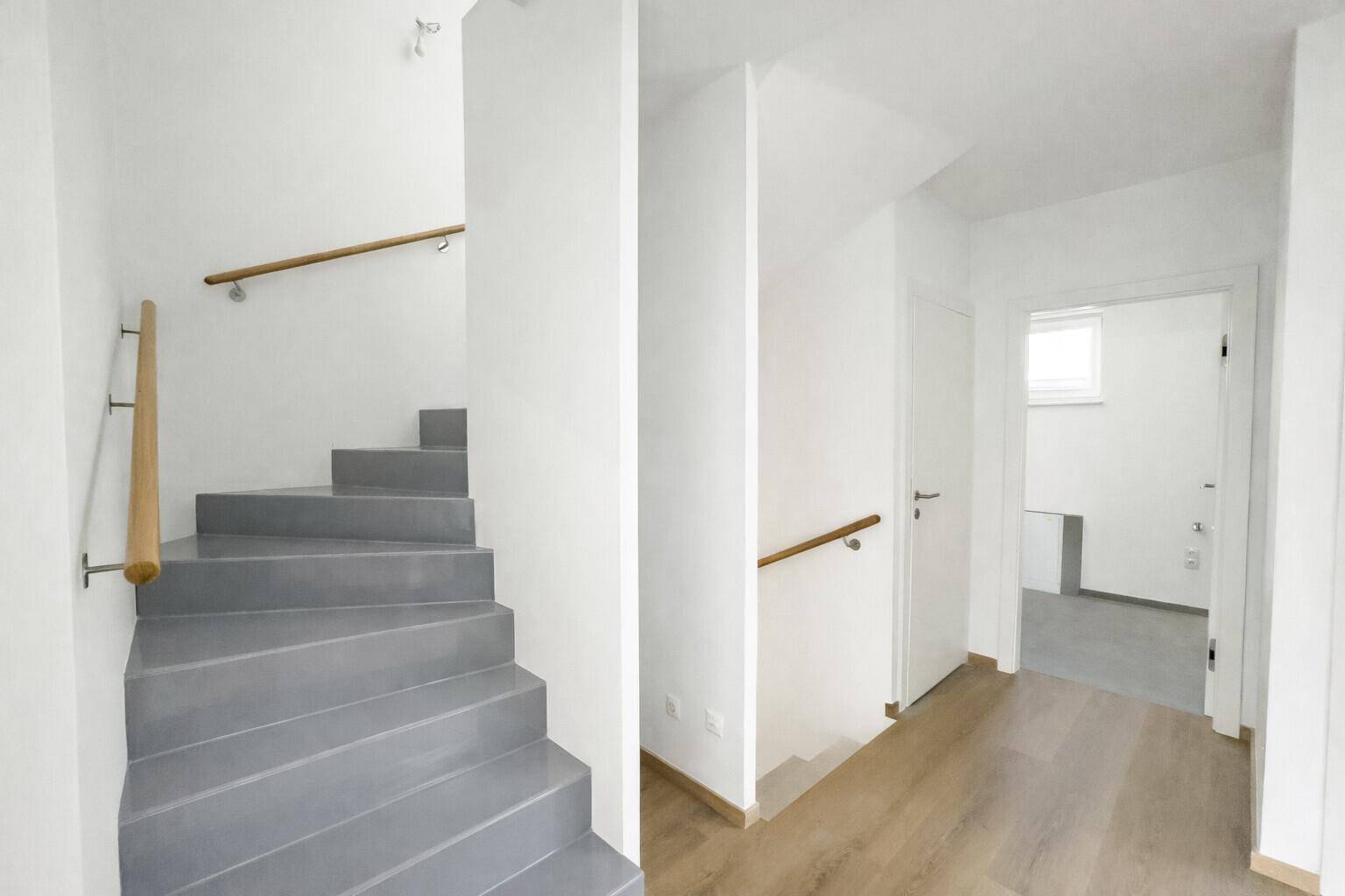 Heller Flur mit moderner Treppe und Holzhandlauf, der die verschiedenen Etagen verbindet.