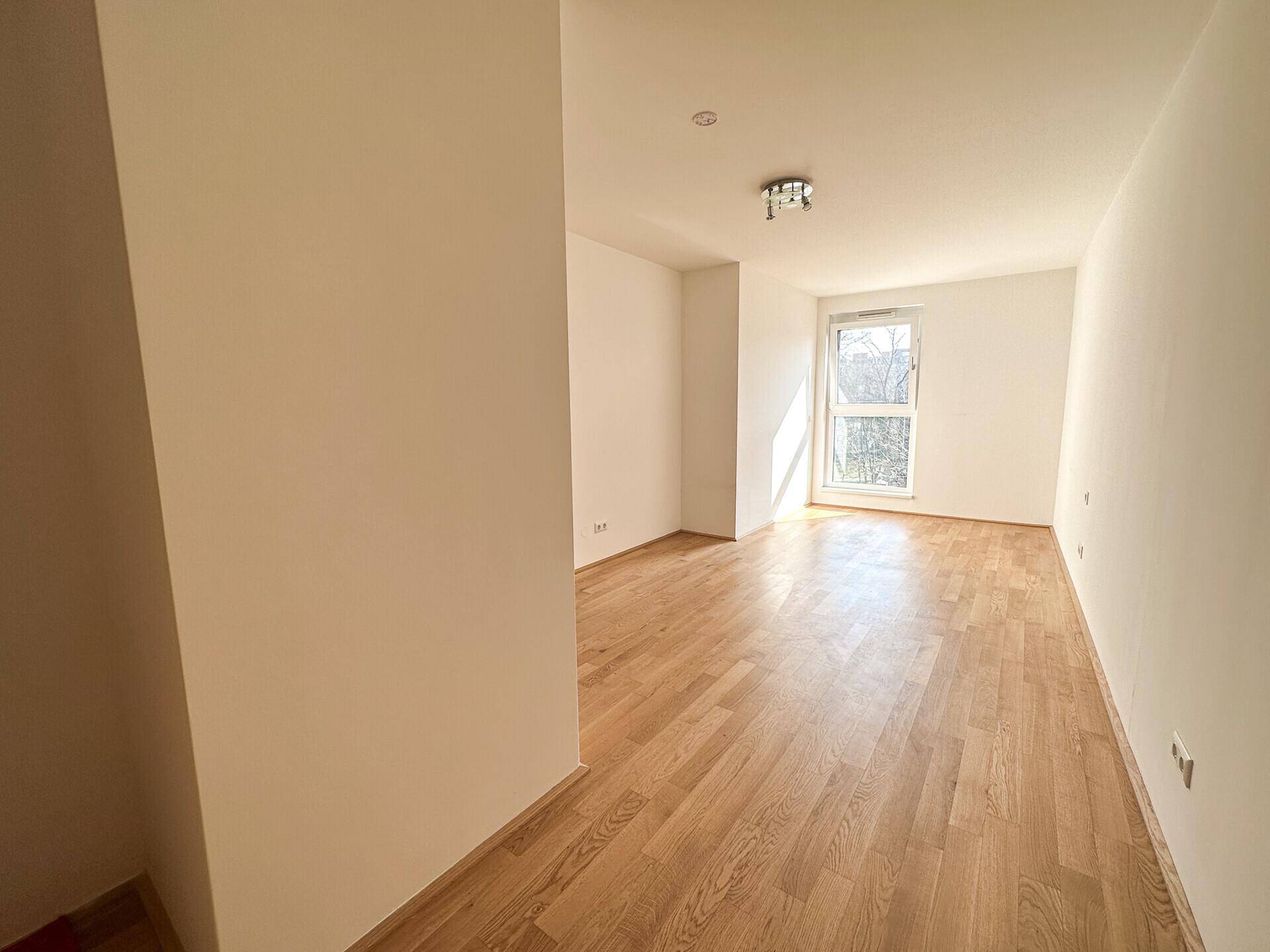 Geräumiges Zimmer mit hellem Parkettboden und einem Fenster, das den Raum erhellt.