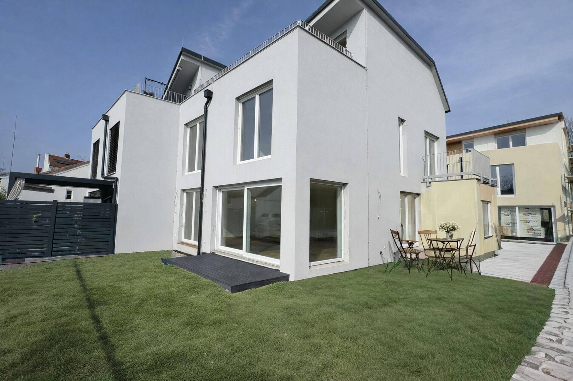 Ansicht eines modernen Hauses mit grünem Rasen, Terrasse und Gartenmöbeln im Freien.