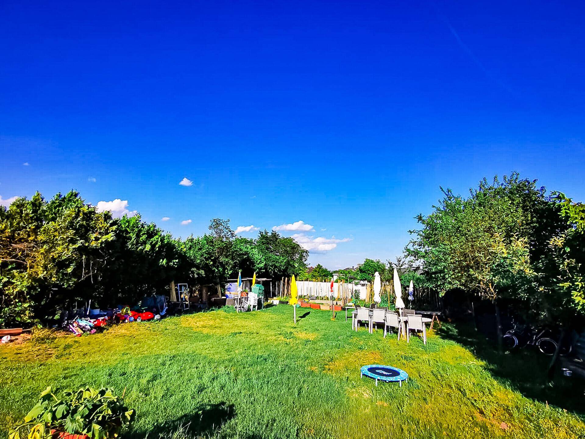 Weitläufiger Garten mit großer Rasenfläche, Sitzbereich und Trampolin unter klarem Himmel.