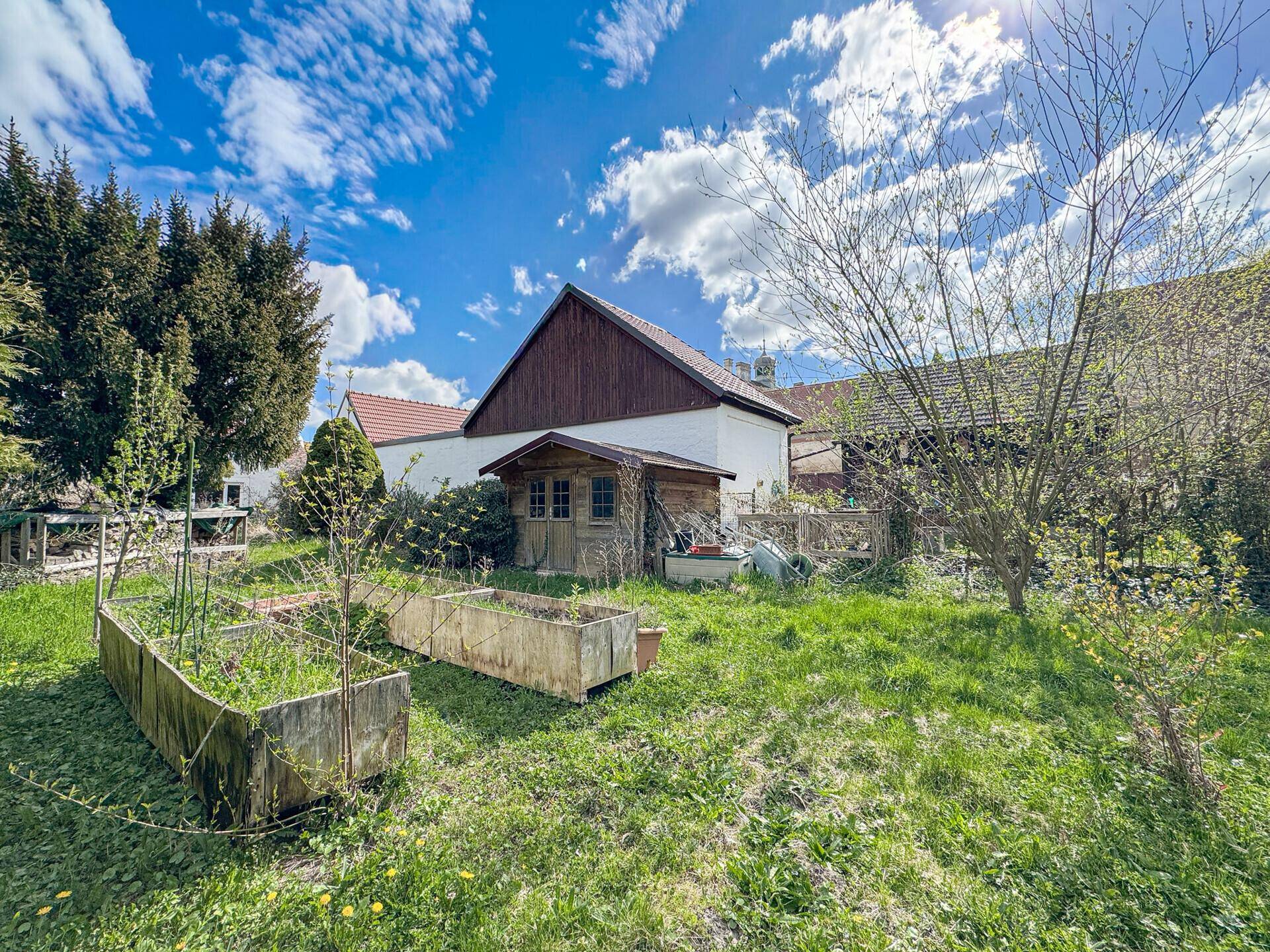 Großer Gartenbereich mit Hochbeeten, einem kleinen Gartenhaus und viel Grünfläche.