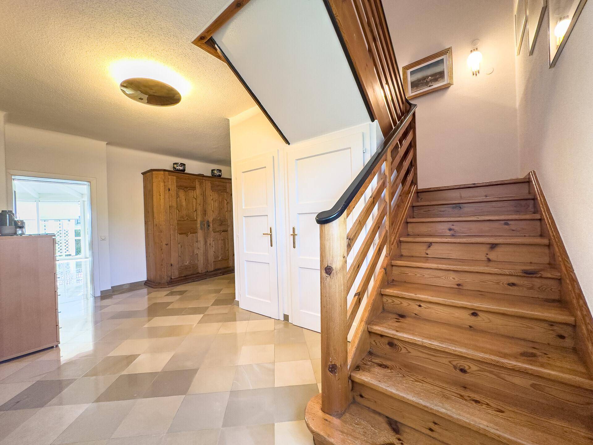 Heller Flur mit Holztreppe, Fliesenboden und traditionellen Holzmöbeln.