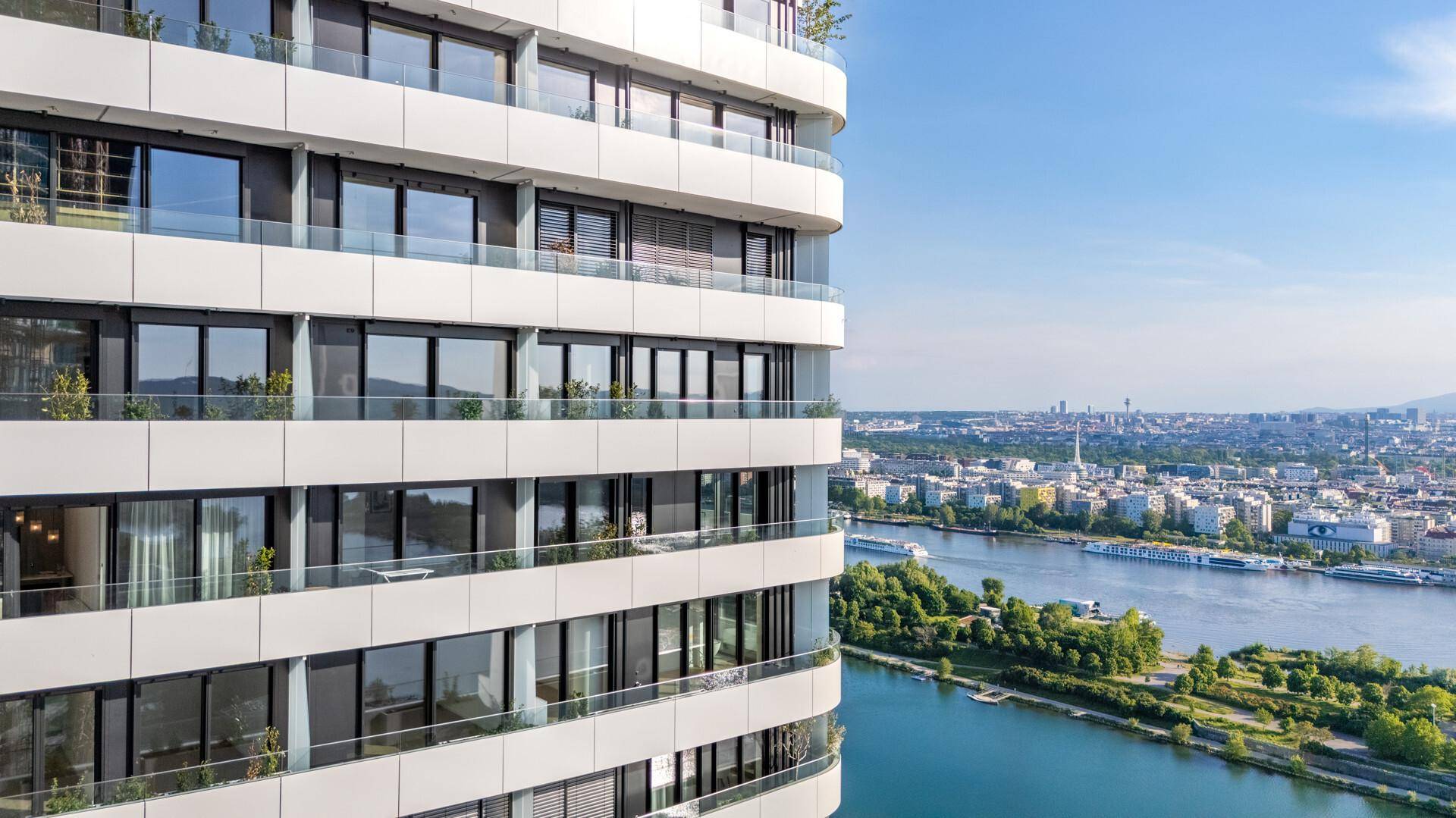 Elegante Fassade eines modernen Wohngebäudes mit zahlreichen Balkonen und weitem Stadtblick über den Fluss.