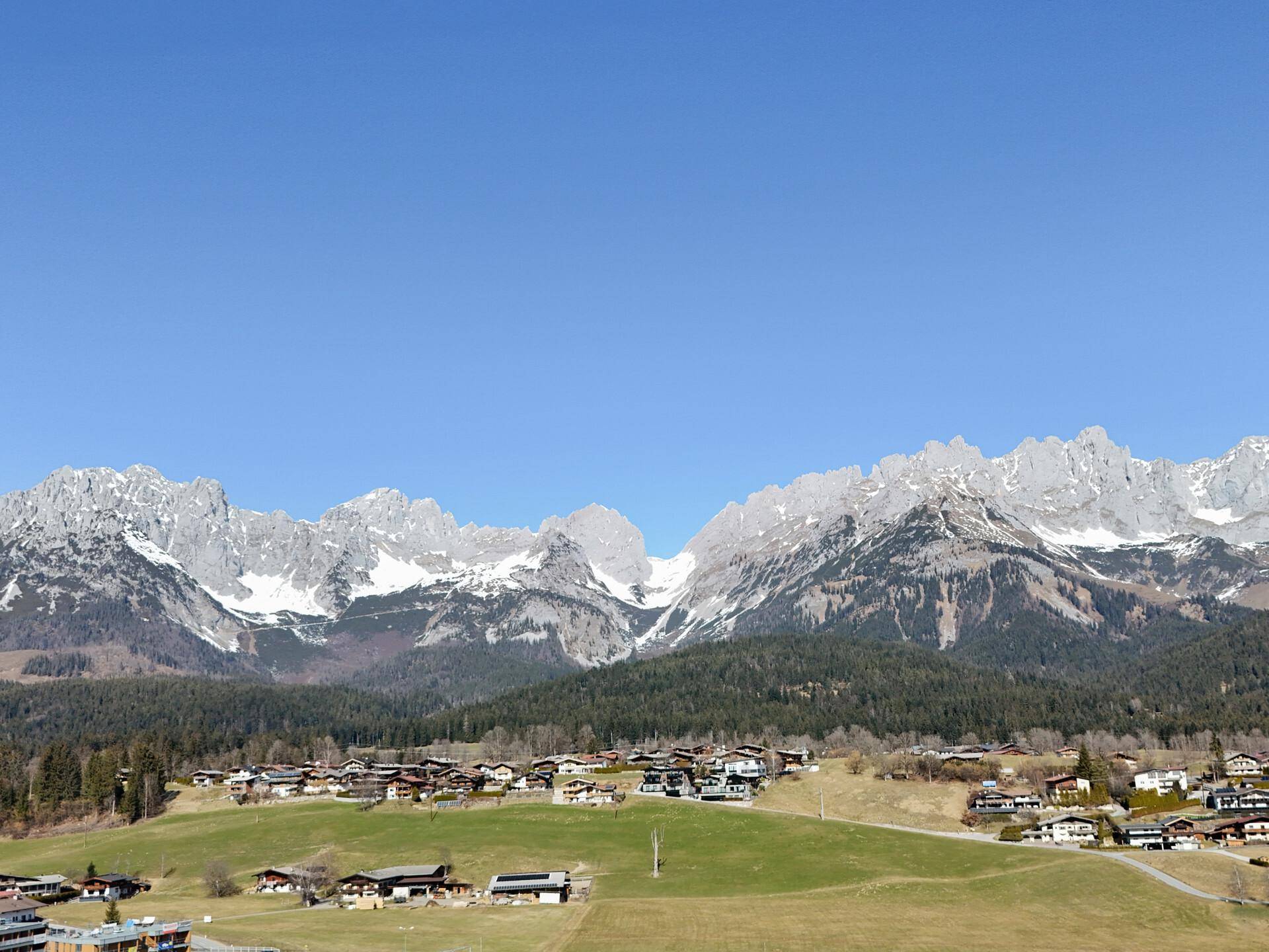 Weitläufiger Blick auf die imposante Bergkette mit schneebedeckten Gipfeln und einem darunterliegenden Dorf.
