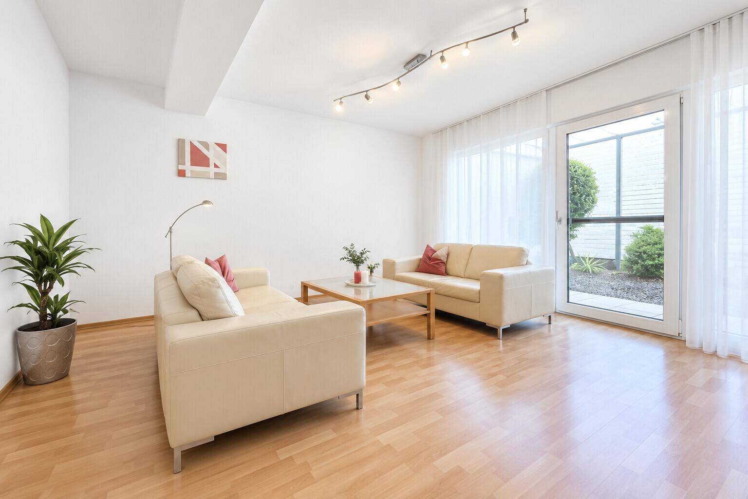 Helles Wohnzimmer mit zwei beigen Sofas, Holzboden und Zugang zu einem Außenbereich.