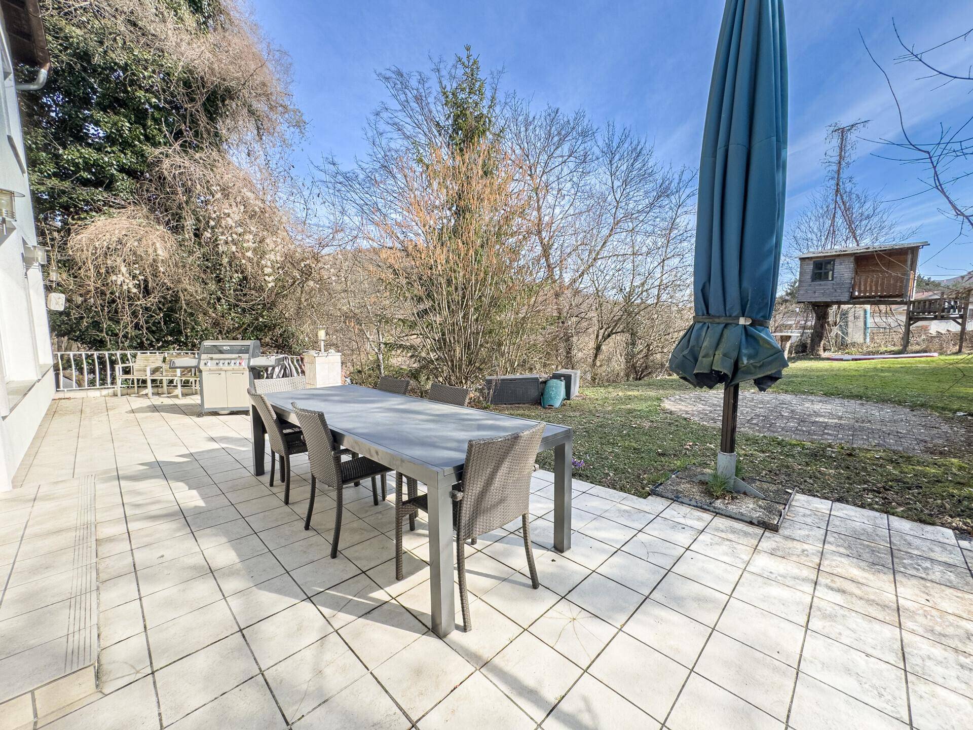 Geräumige Terrasse mit großem Esstisch und Grill, umgeben von viel Grün.