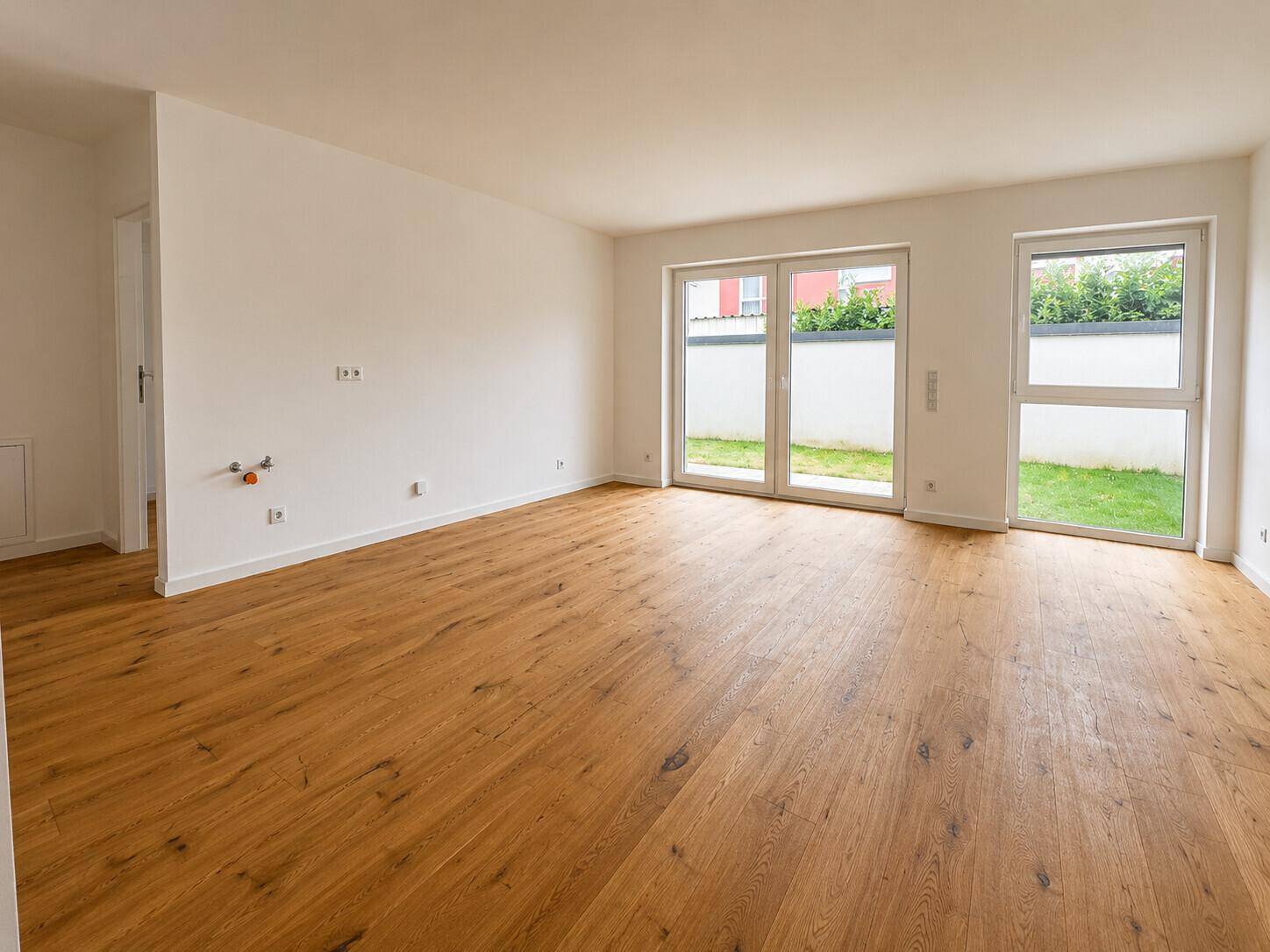 Heller Raum mit Holzboden und Zugang zu einem kleinen Gartenbereich, ideal für eine offene Küche oder Wohnzimmer.