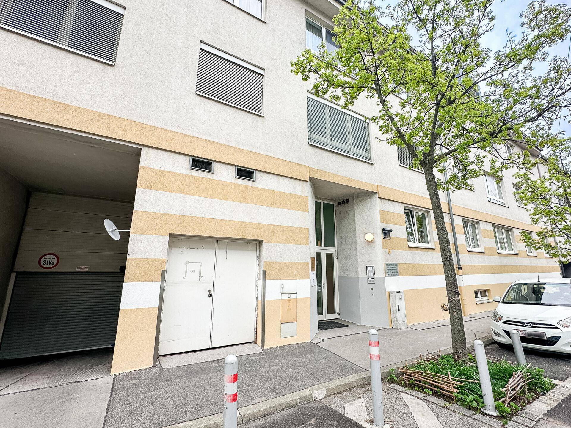 Fassade eines Mehrfamilienhauses mit Garageneinfahrt und Parkmöglichkeiten an der Straße.