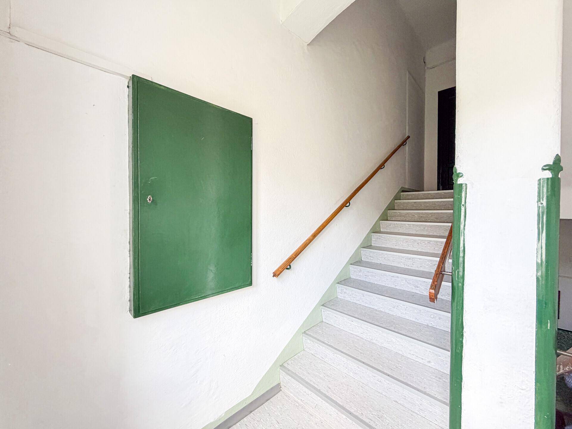 Treppenhaus mit Holzgeländer und einem grünen Wandschrank, der zur nächsten Etage führt.