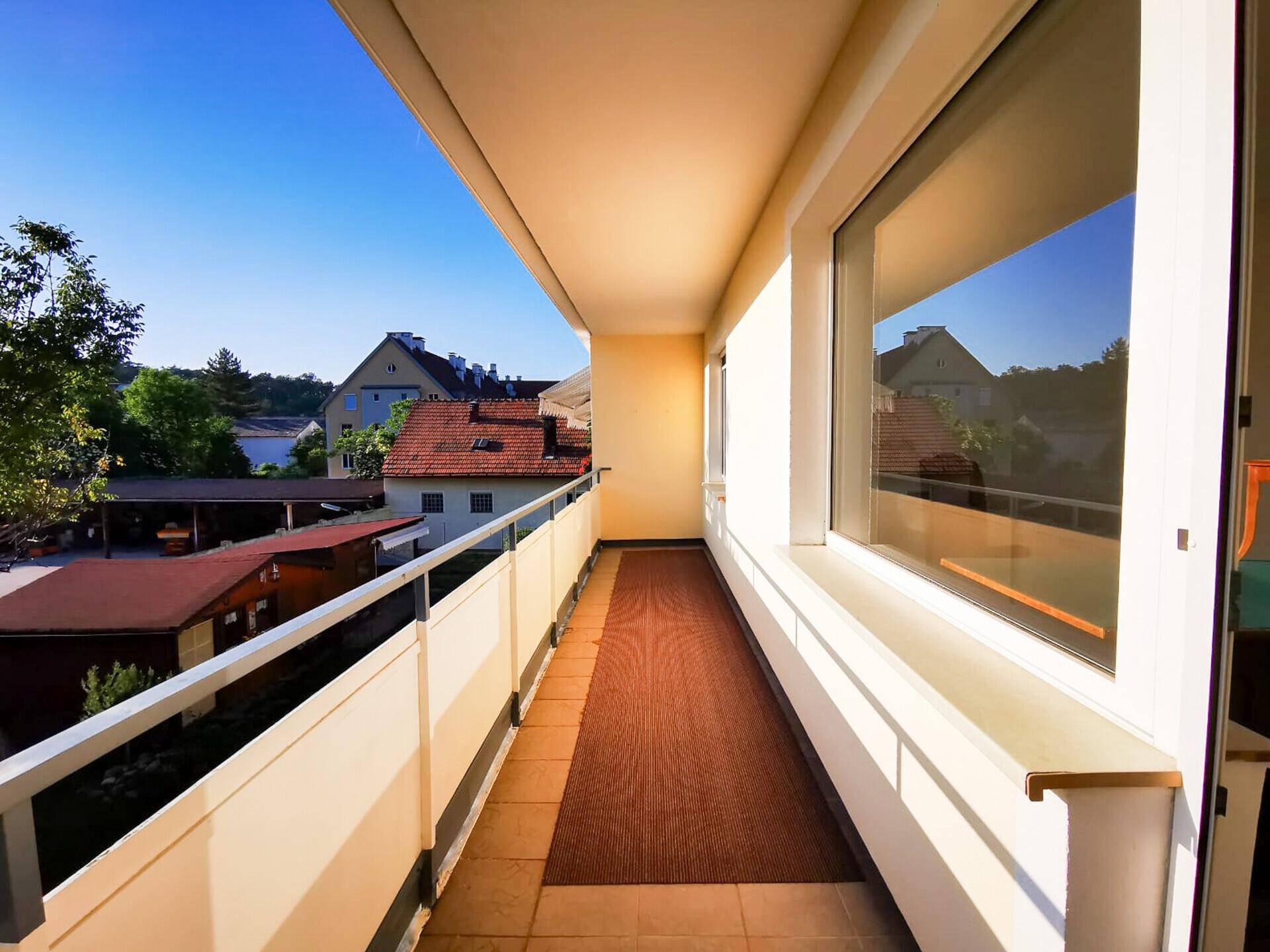 Langer, schmaler Balkon mit Fliesenboden und Blick auf die umliegenden Häuser.