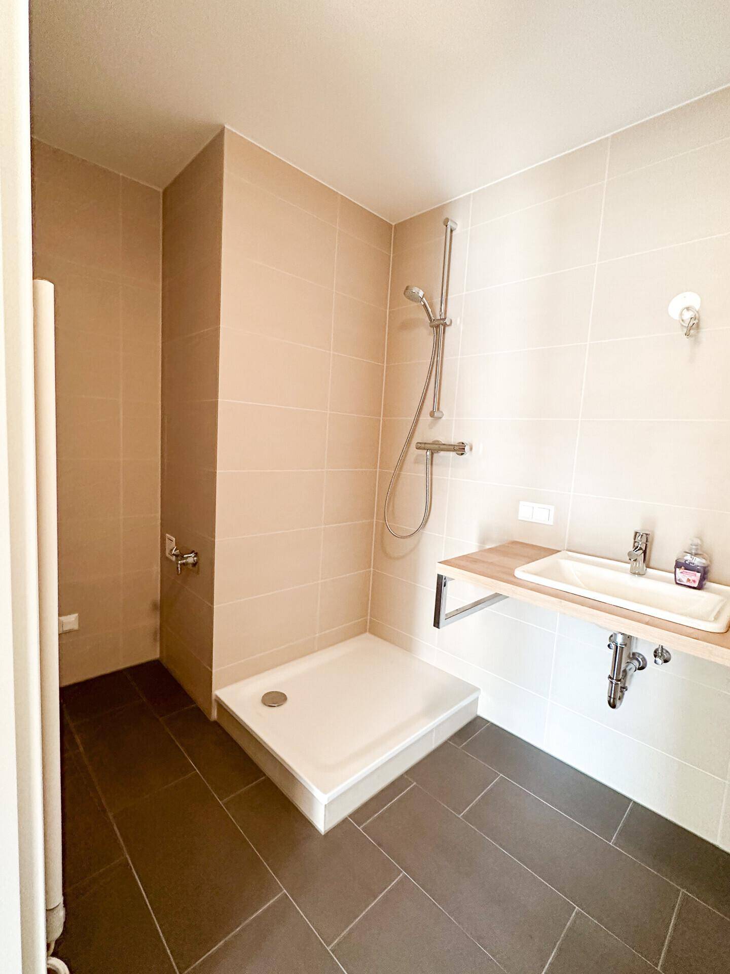 Modernes Badezimmer mit beigen Wandfliesen, dunklem Boden und einer Duschkabine.