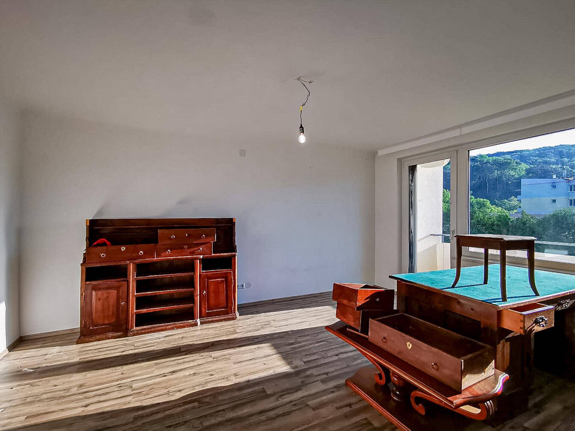 Heller Wohnraum mit Holzboden, großen Fenstern und Zugang zu einem Außenbereich.