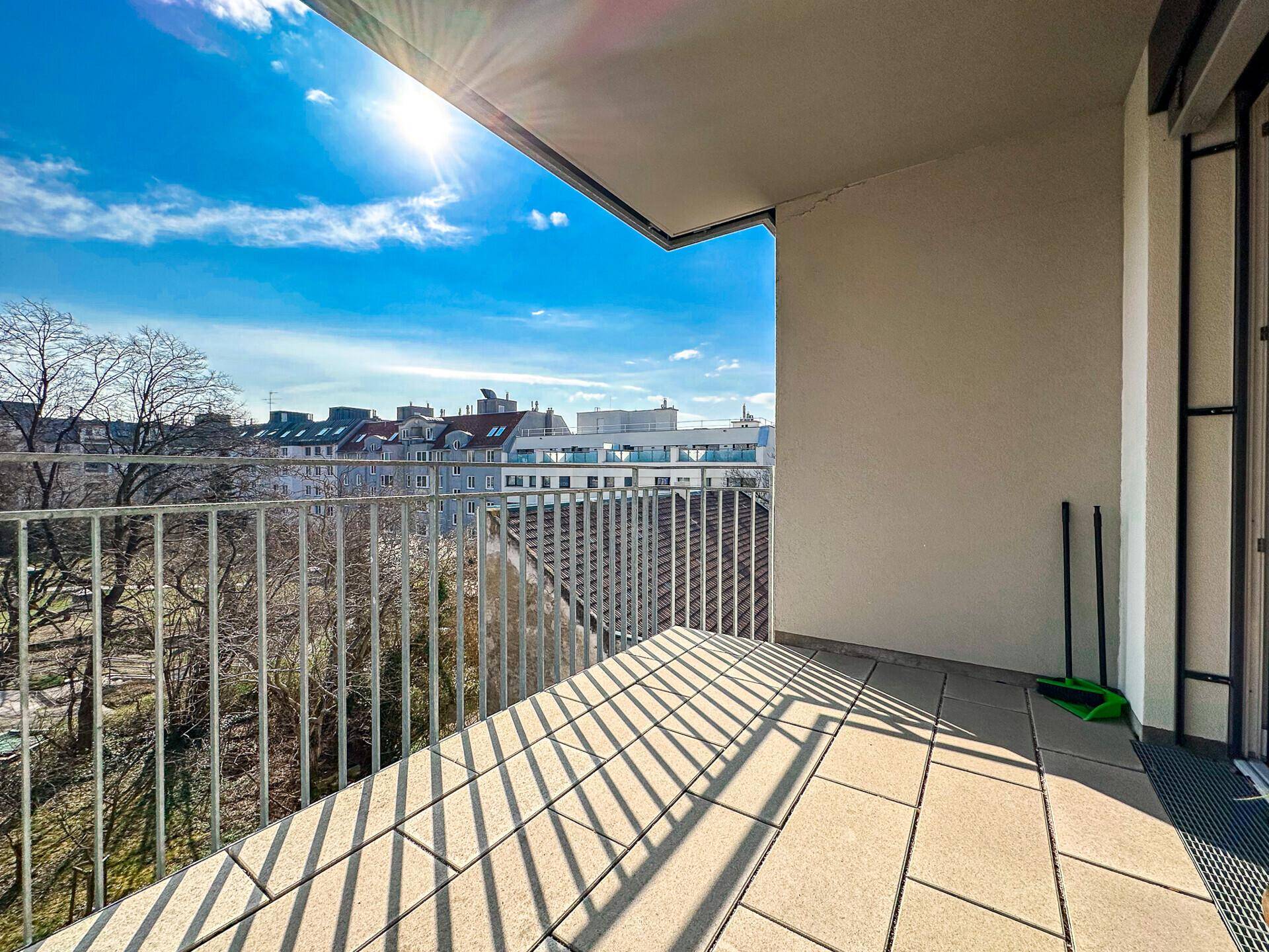 Heller Balkon mit Fliesenboden und weitem Blick über die Stadt und grüne Bäume.