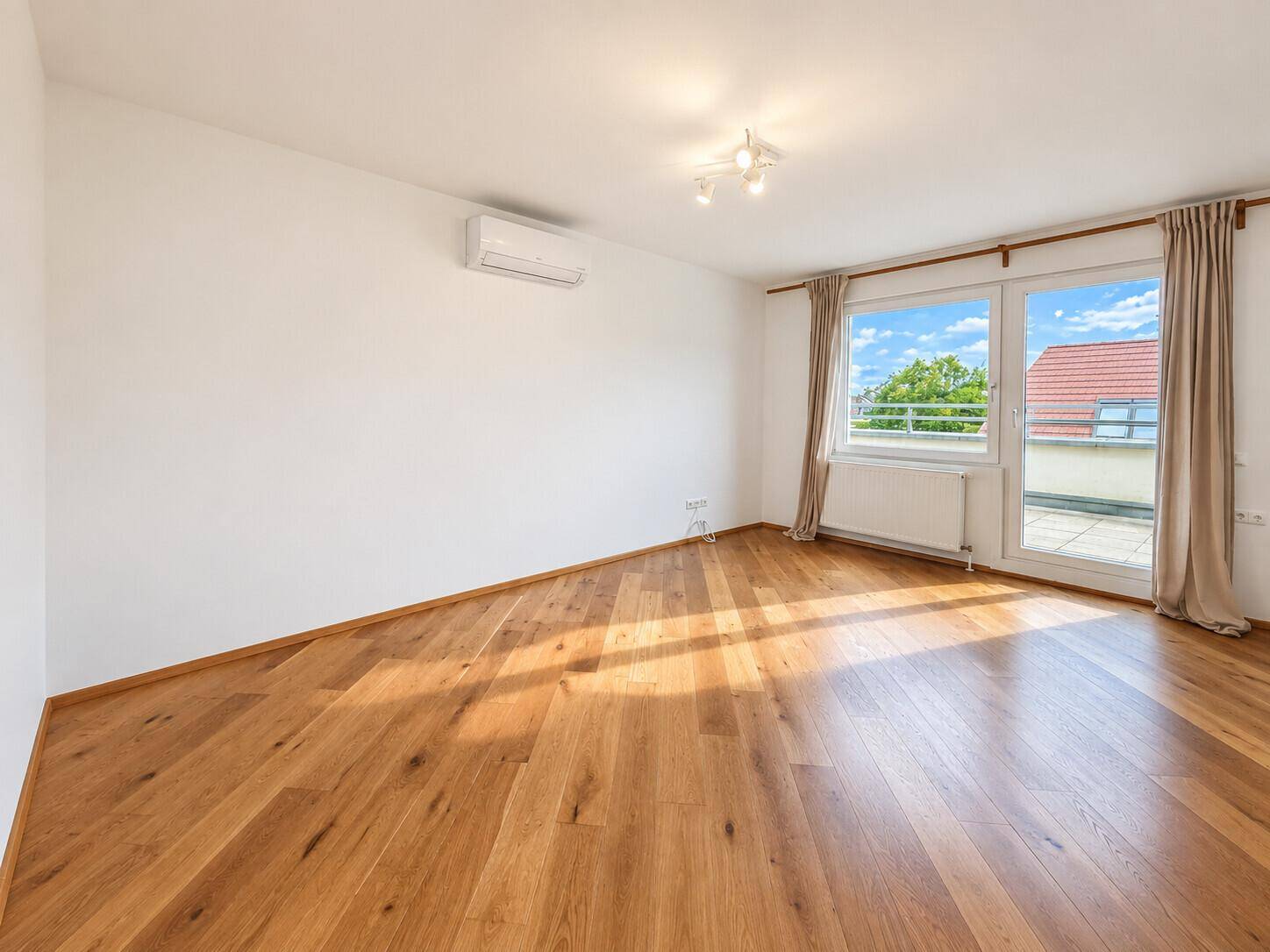 Geräumiges Zimmer mit Holzboden, Klimaanlage und Zugang zu einem Außenbereich.