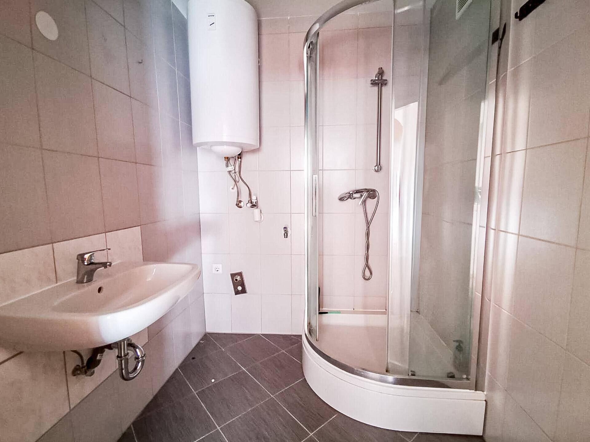 Gefliestes Badezimmer mit Duschkabine, Waschbecken und Warmwasserboiler.