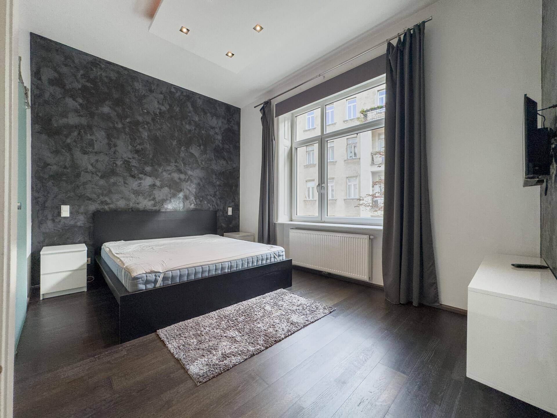 Modernes Schlafzimmer mit dunklem Holzboden, einer Akzentwand und großem Fenster mit Blick nach draußen.