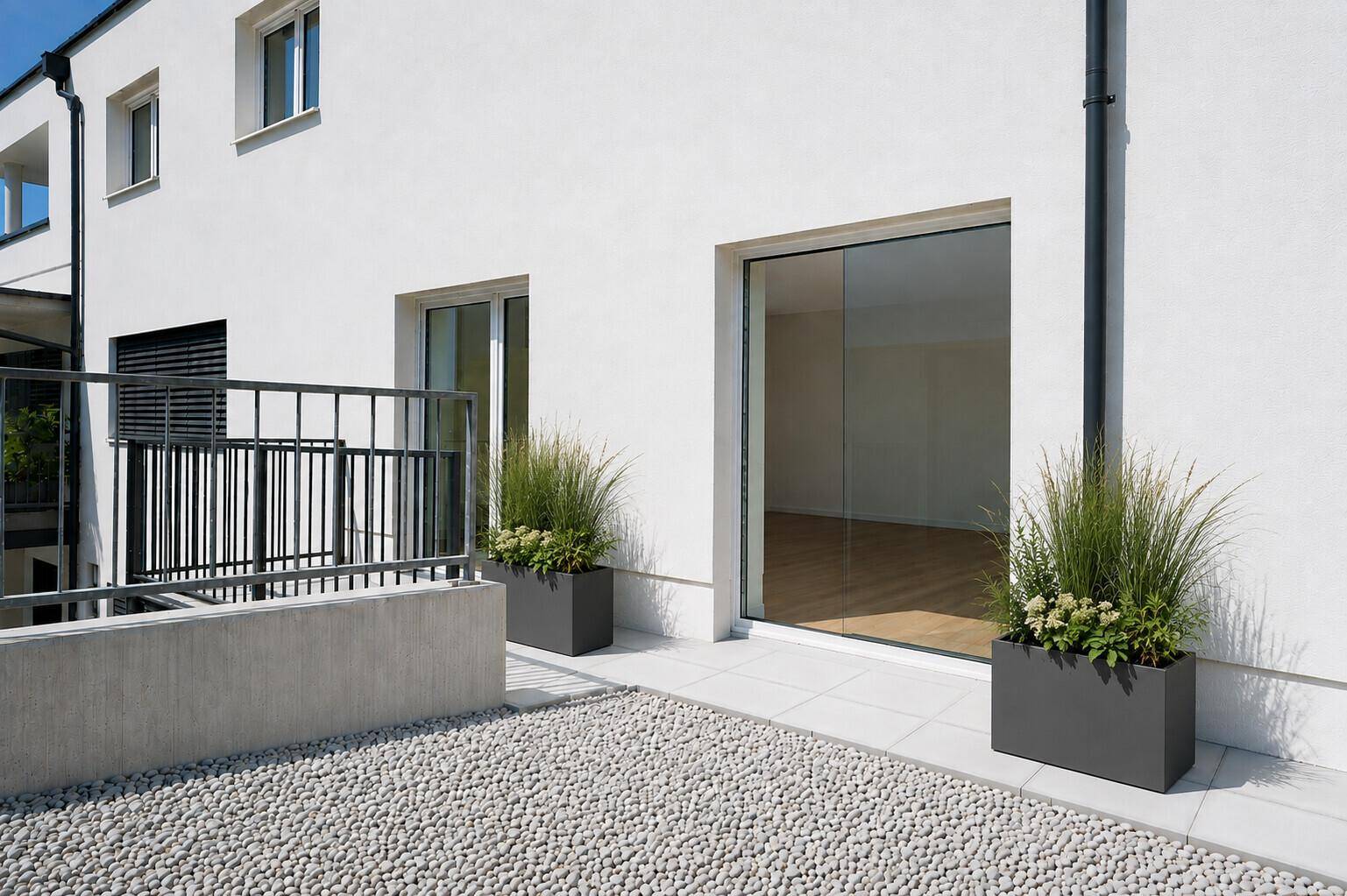 Kleine, moderne Terrasse mit weißen Kieselsteinen und großen Glasschiebetüren zum Innenbereich.
