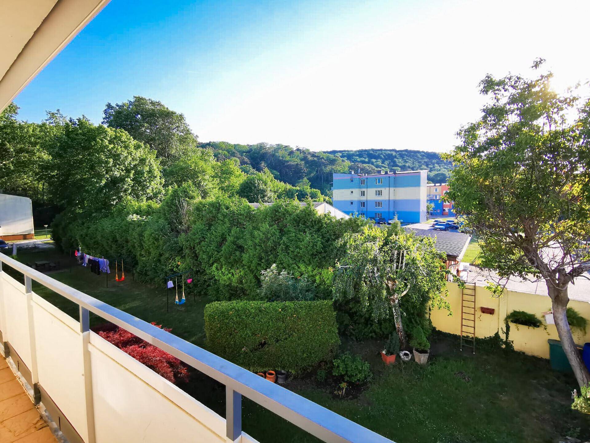 Blick vom Balkon auf einen grünen Gartenbereich und die umliegende Bebauung.