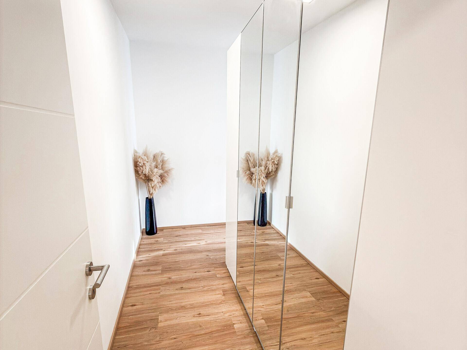 Heller Flur mit Spiegelschränken und Holzboden, der zu einem weiteren Raum führt, modern und funktional.