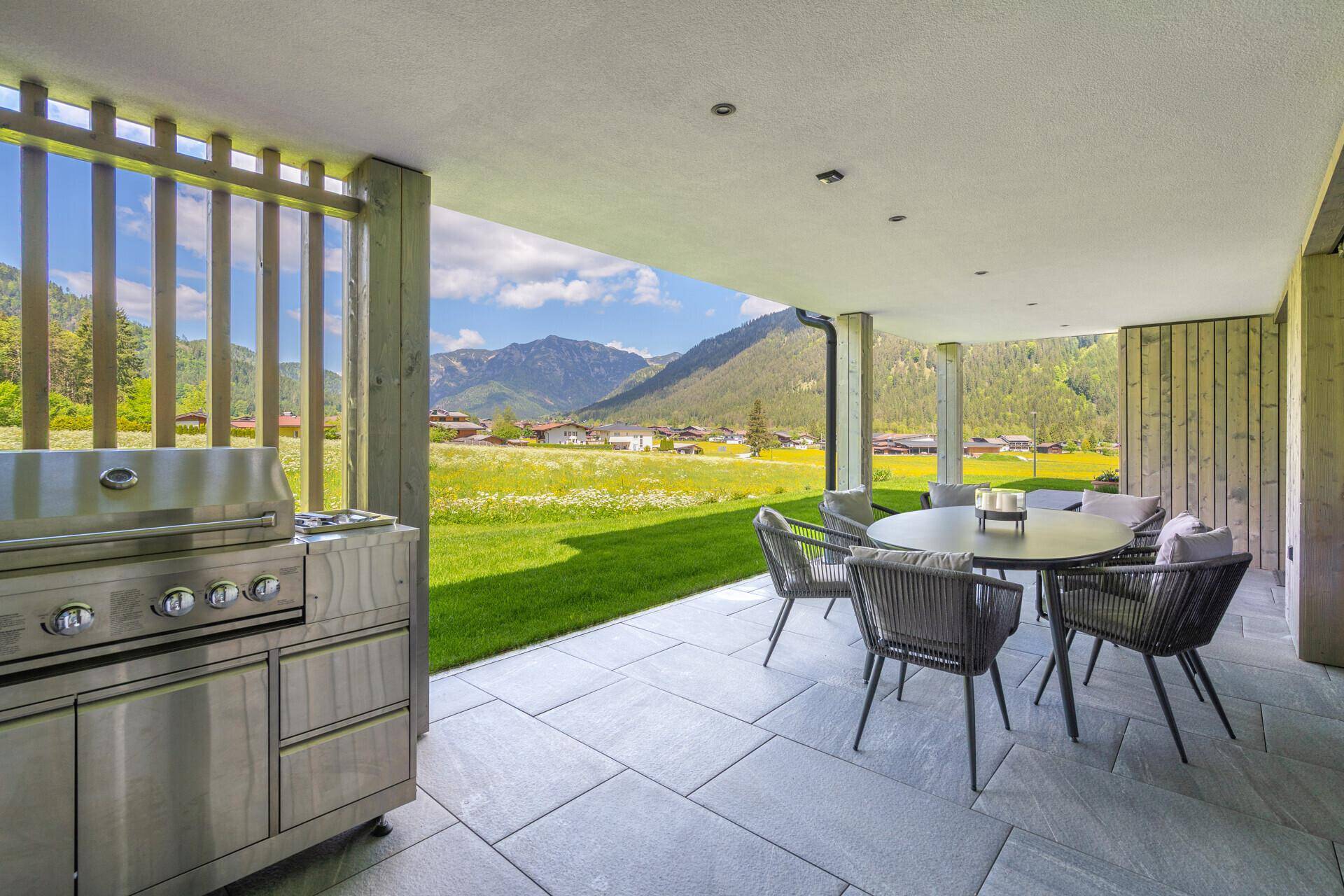 Überdachte Terrasse mit Außenküche, Essbereich und weitem Blick auf die Berge und Natur.
