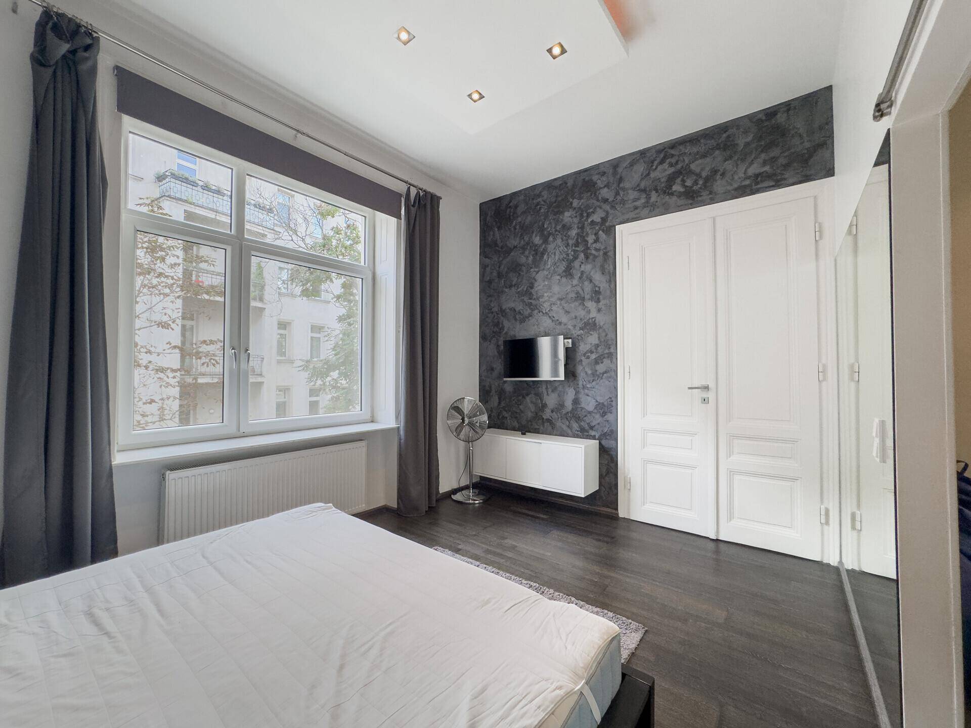 Helles Schlafzimmer mit dunklem Holzboden, integriertem Fernseher und Spiegelschränken an der Wand.