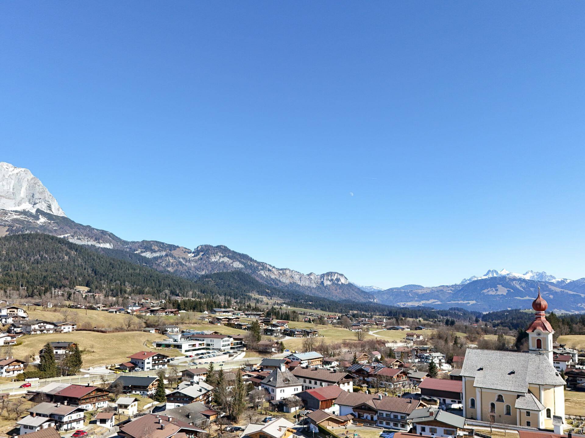 Idyllische Landschaft mit einem Dorf, einer Kirche und sanften Hügeln unter einem klaren blauen Himmel.