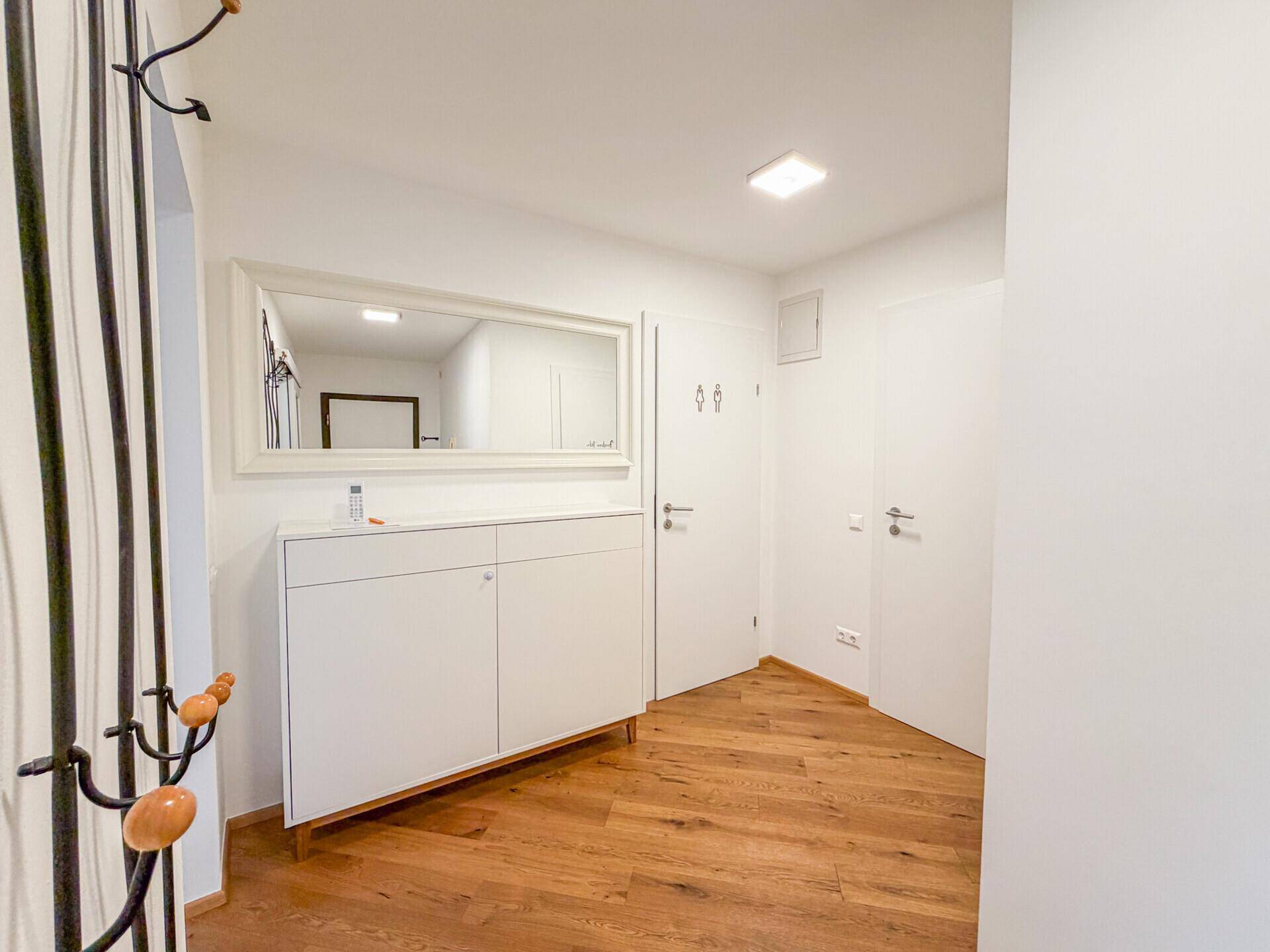 Heller Eingangsbereich mit Holzboden, weißem Schuhschrank und großem Spiegel.