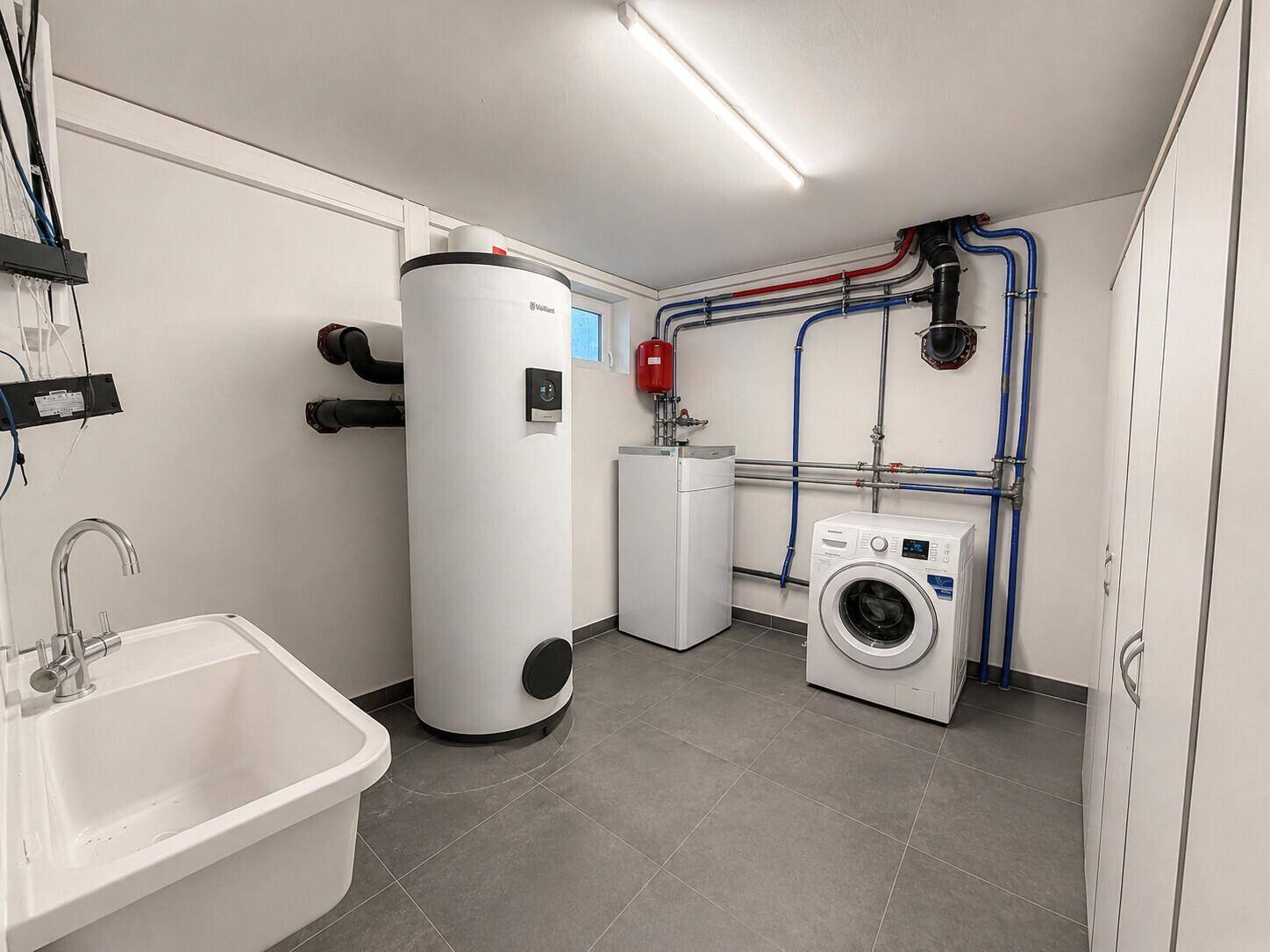 Praktischer Hauswirtschaftsraum im Keller mit Waschmaschine, Spülbecken und Heizungsanlage.