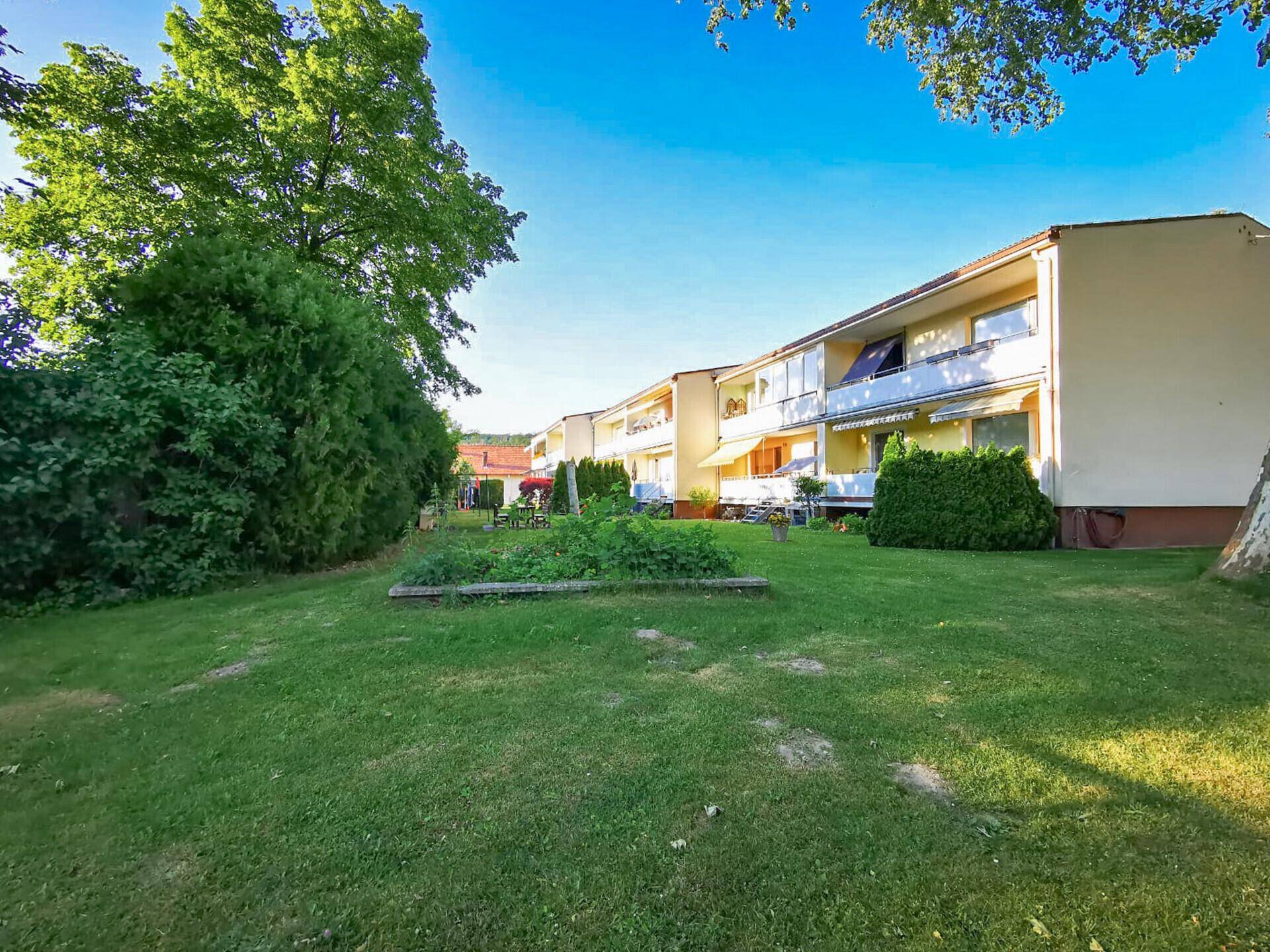 Gepflegter Gemeinschaftsgarten mit Rasenfläche, Beeten und Blick auf die Wohnanlage.
