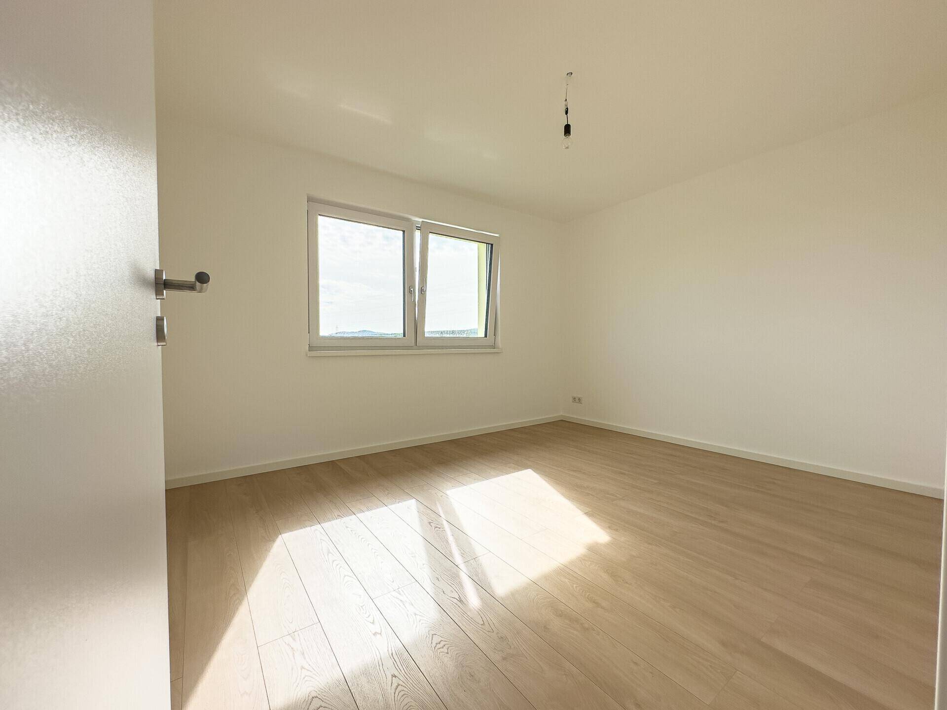 Lichtdurchflutetes Zimmer mit hellem Holzboden und großen Fenstern, ideal für Schlaf- oder Arbeitszimmer.