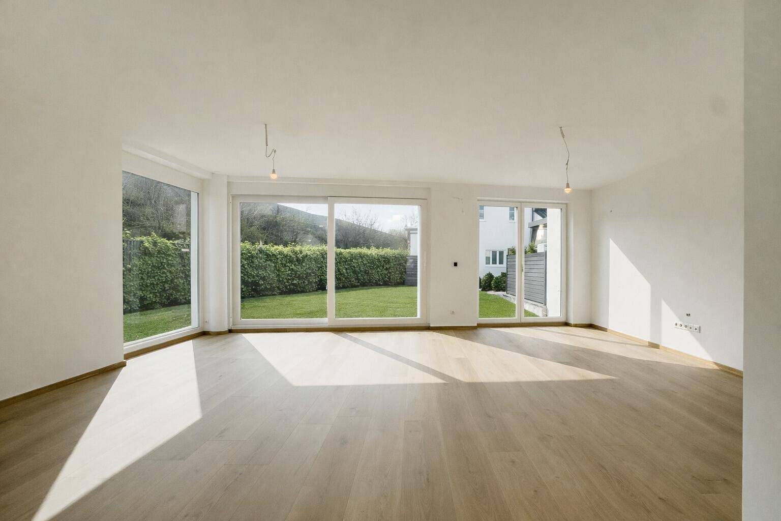 Helles, leeres Wohnzimmer mit großen Fenstern und direktem Zugang zum grünen Garten.