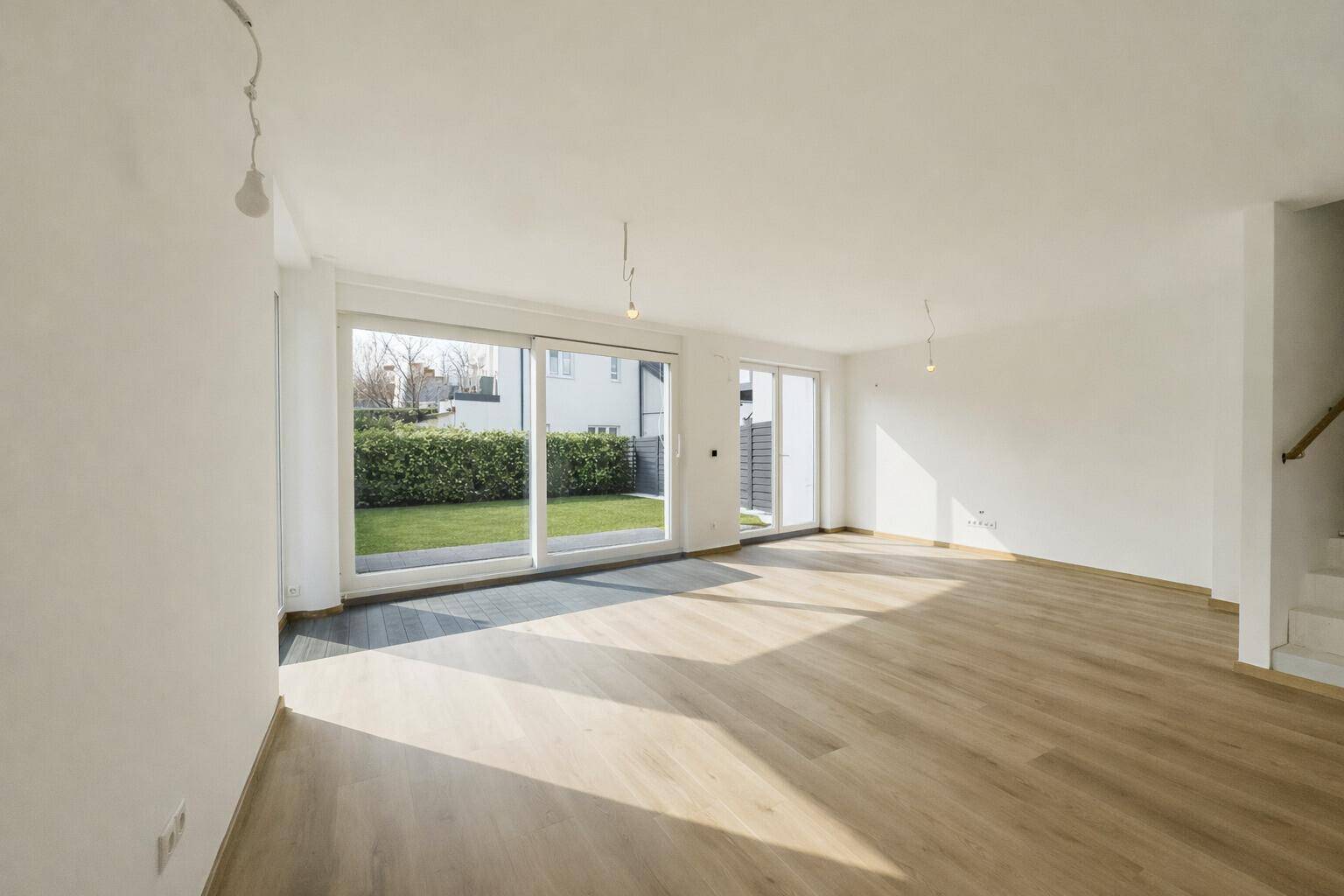 Geräumiges Wohnzimmer mit hellem Holzboden, großen Fenstern und Blick auf den Garten.