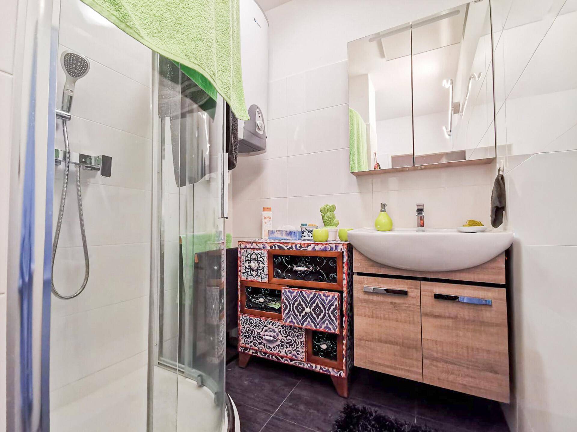 Helles Badezimmer mit Dusche, Waschbecken und einem dekorativen Unterschrank.