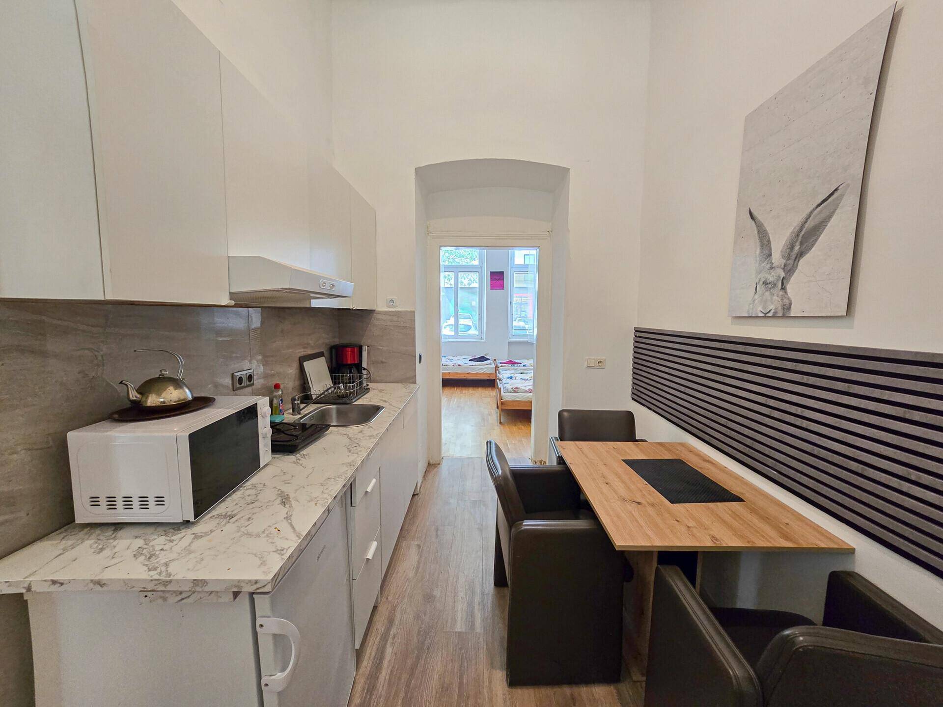 Schmale Küche mit Essbereich und Blick durch einen Torbogen in ein angrenzendes Zimmer.