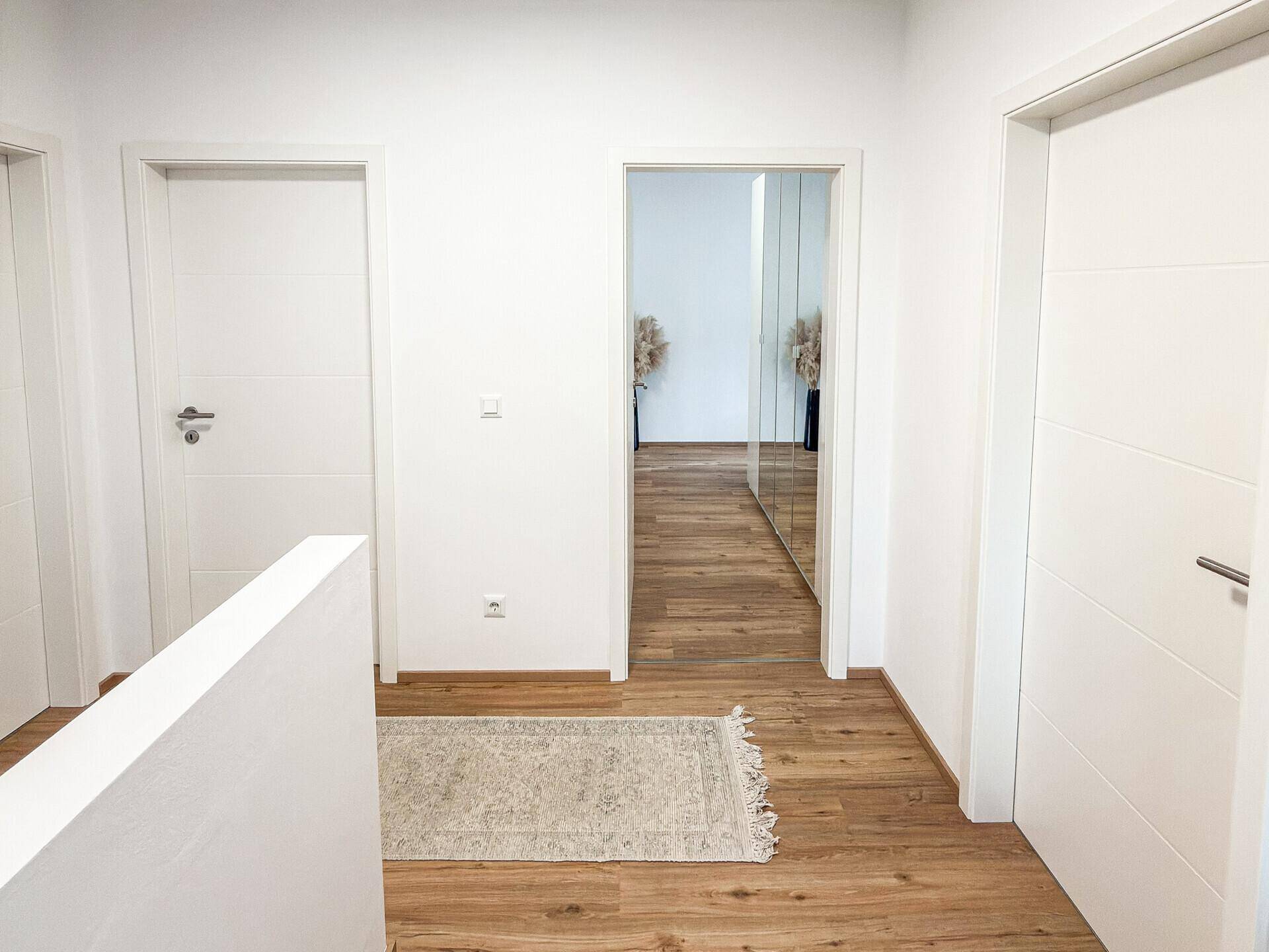 Heller Flur im Obergeschoss mit Holzboden und Zugang zu mehreren Zimmern, modern und funktional.