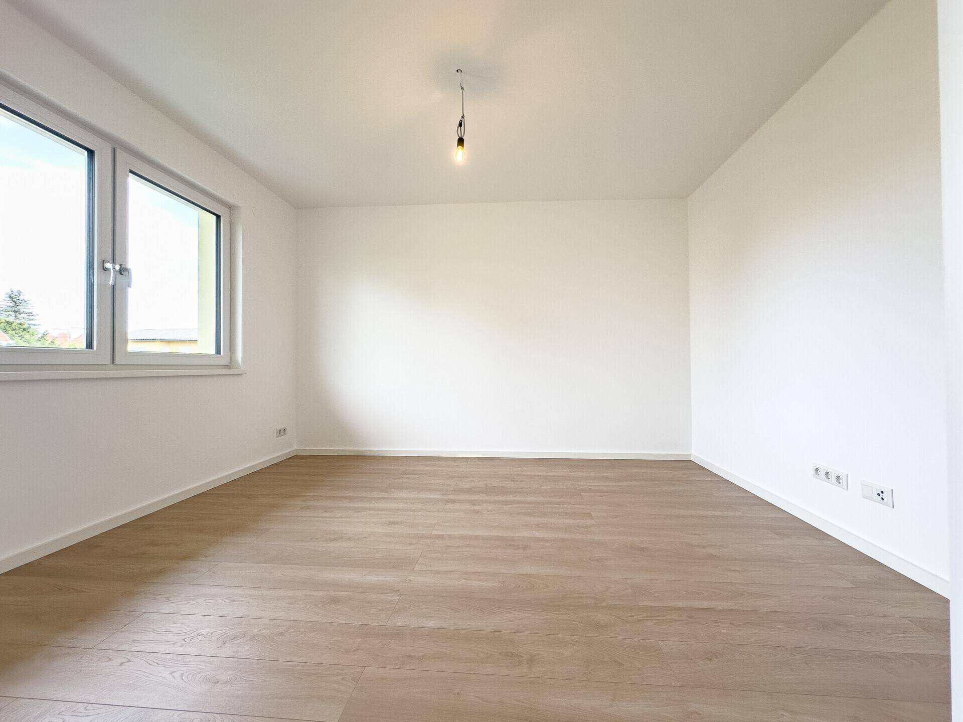 Helles, leeres Zimmer mit Holzboden und zwei Fenstern, bereit zur individuellen Gestaltung.