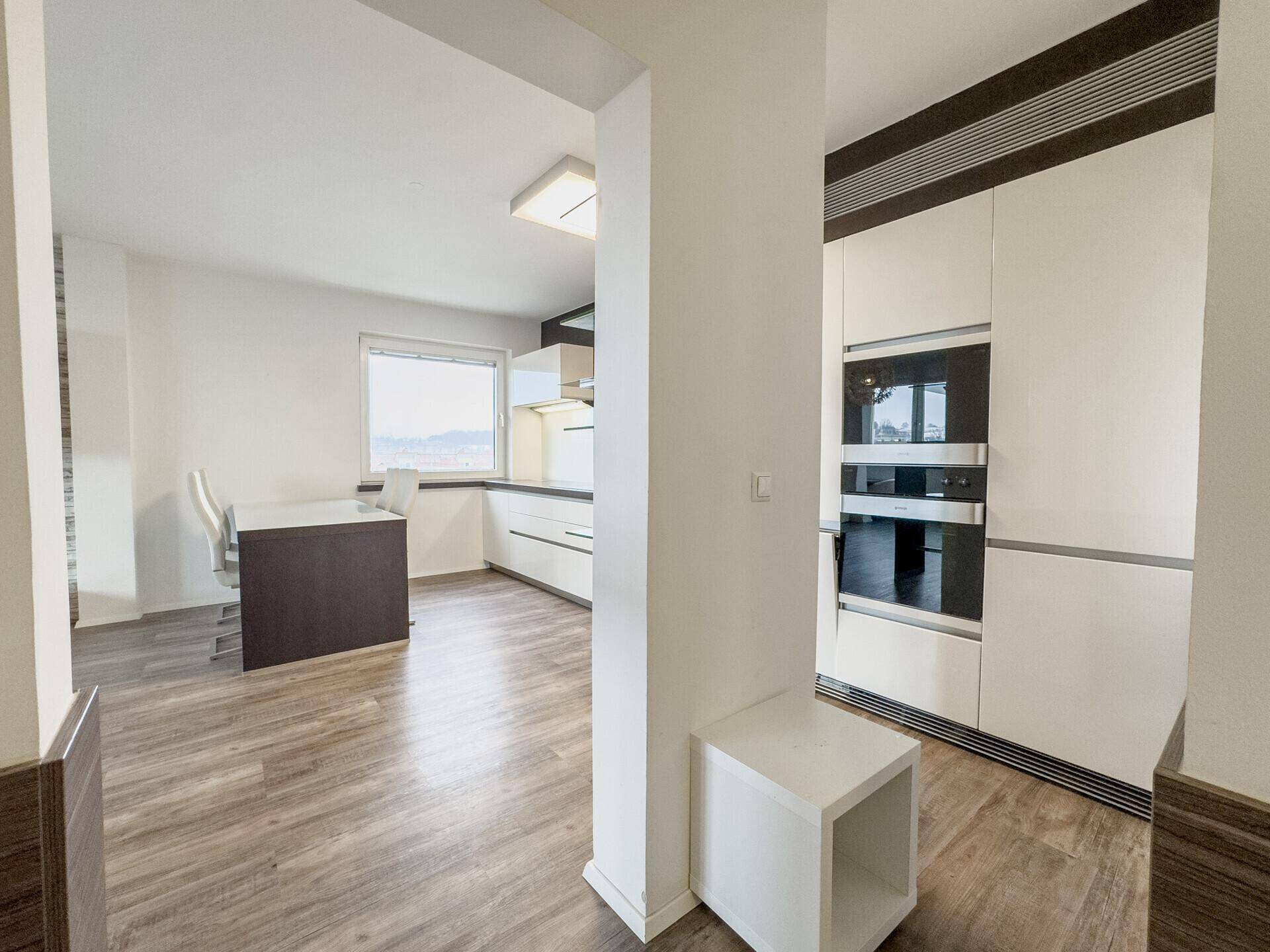 Moderne Einbauküche mit integrierten Geräten und hellem Laminatboden, offen zum Essbereich.