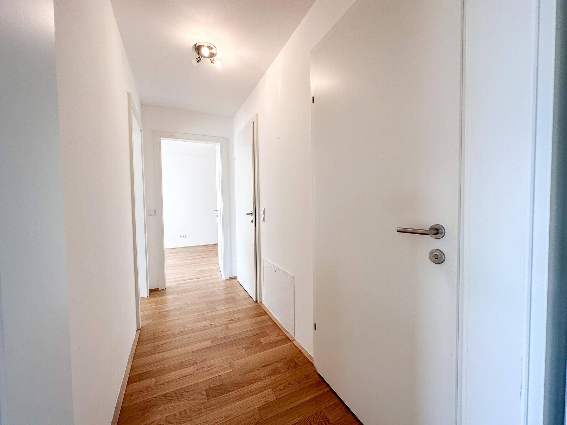 Heller Flur mit modernem Holzboden und weißen Türen, der zu weiteren Räumen führt.