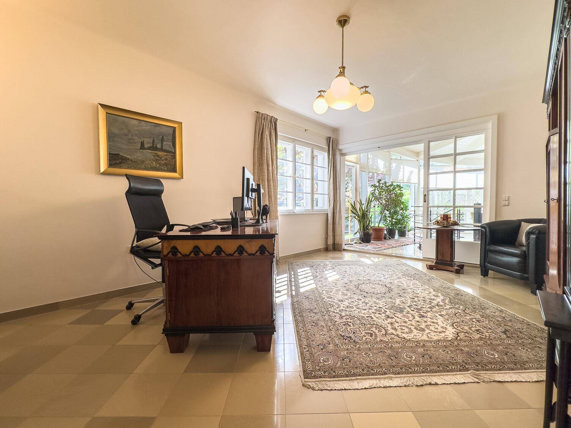 Helles Arbeitszimmer mit Schreibtisch, Teppich und Zugang zum Wintergarten.
