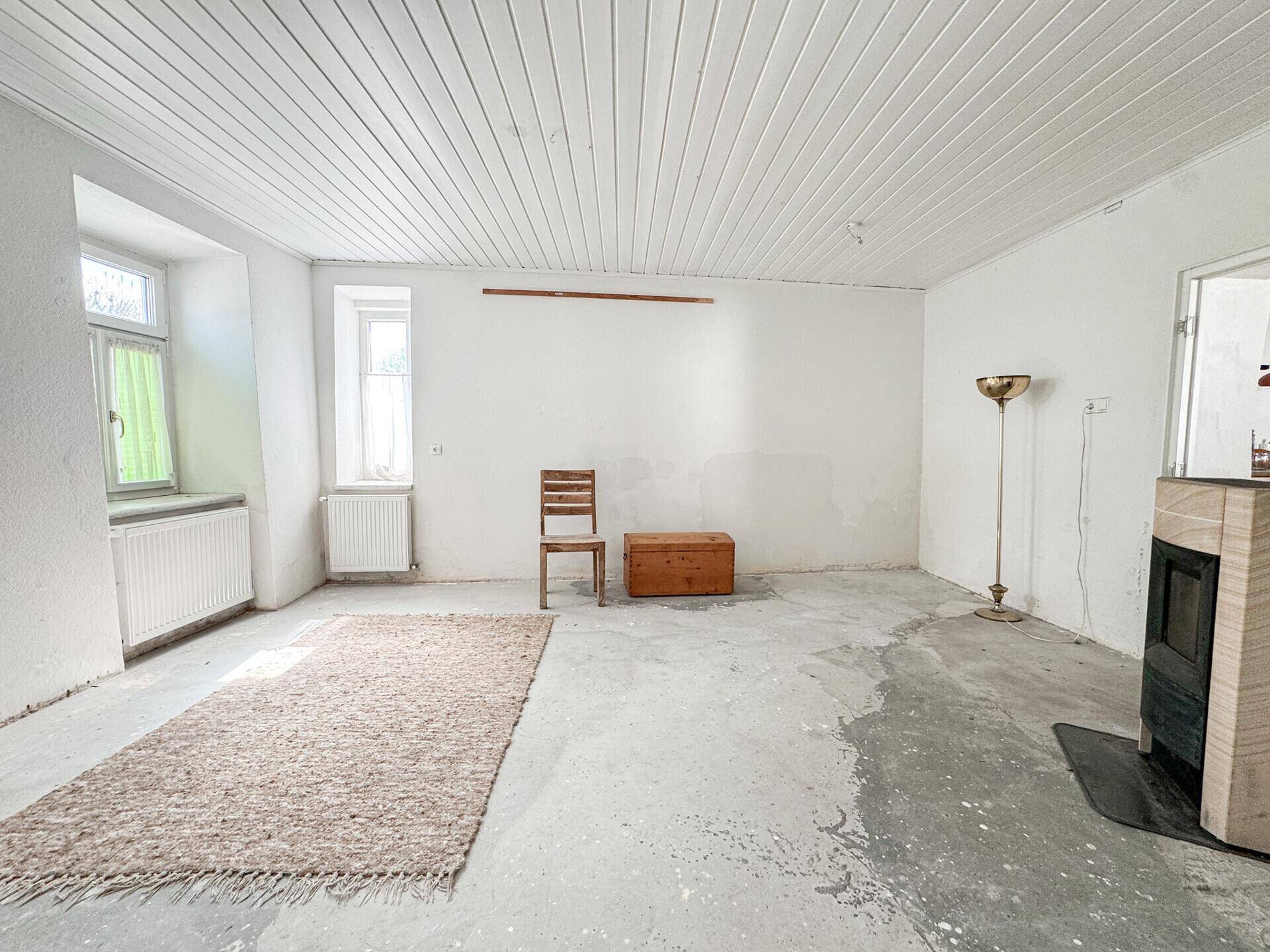 Geräumiger, unmöblierter Raum mit Betonboden und einem Kaminofen, bereit zur Gestaltung.