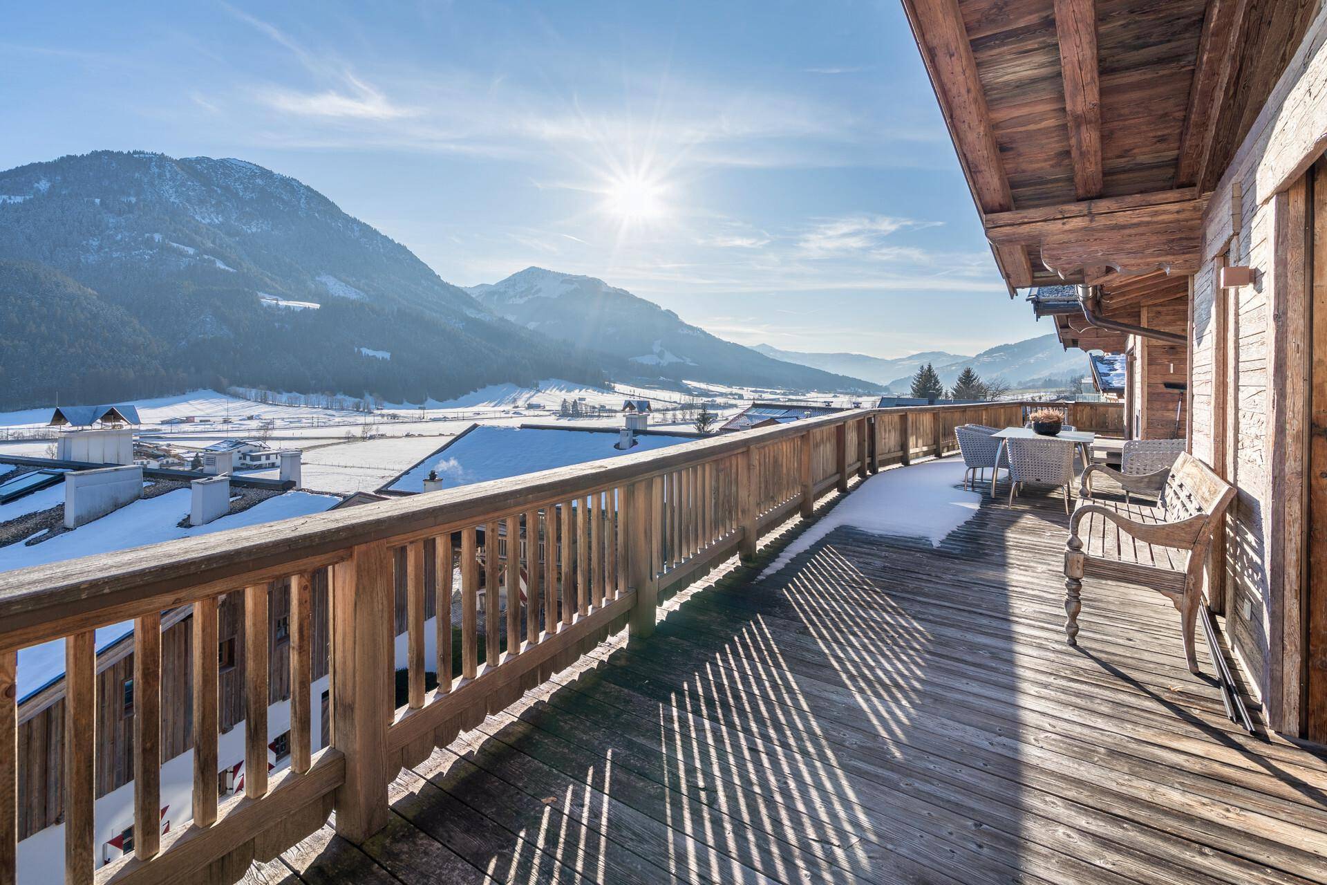 Großer Holzbalkon mit Sitzgelegenheiten und atemberaubendem Panoramablick auf die verschneite Bergwelt.