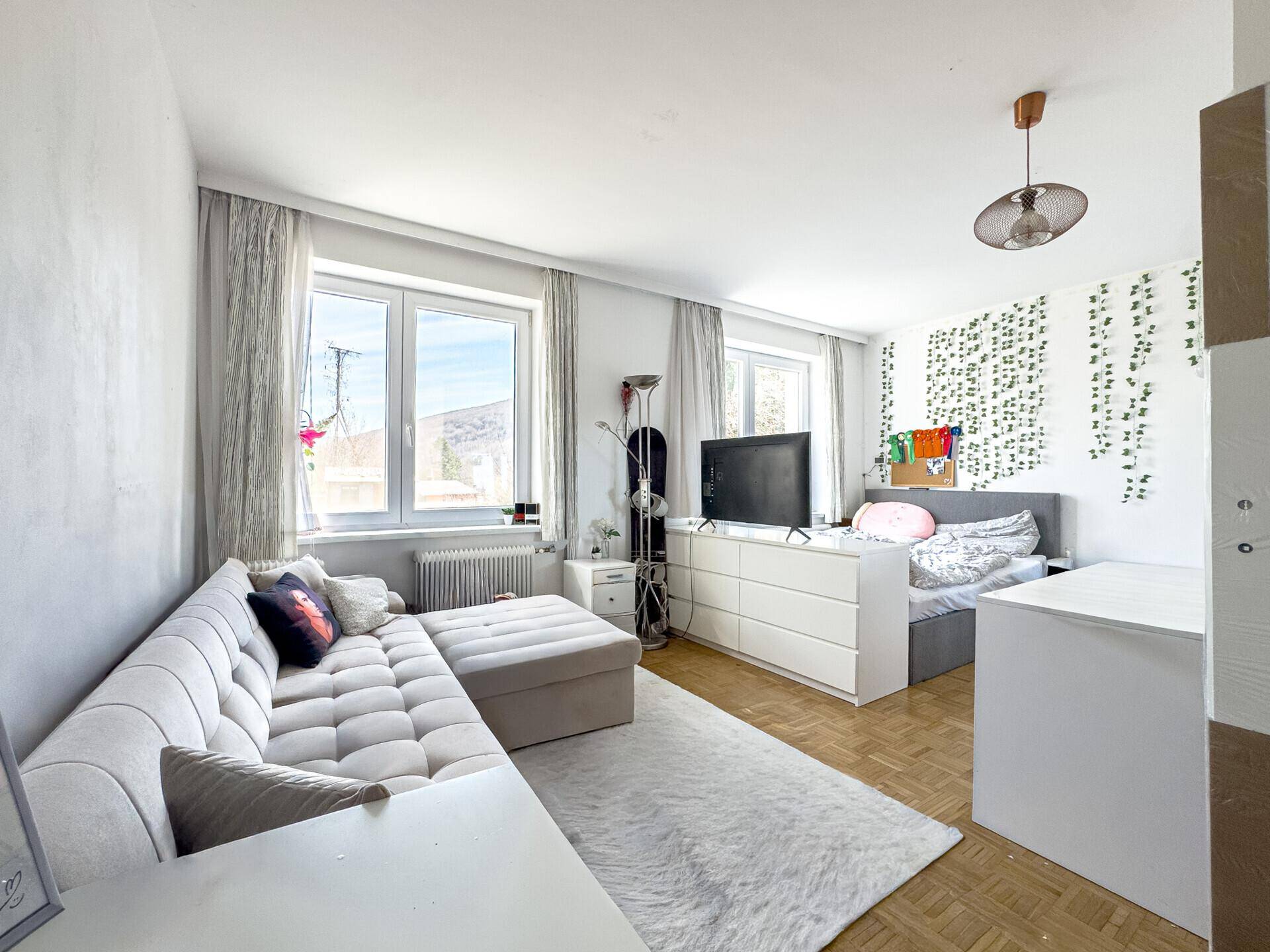 Gemütliches Schlafzimmer mit Sofa, Bett und Fenstern für natürliches Licht.