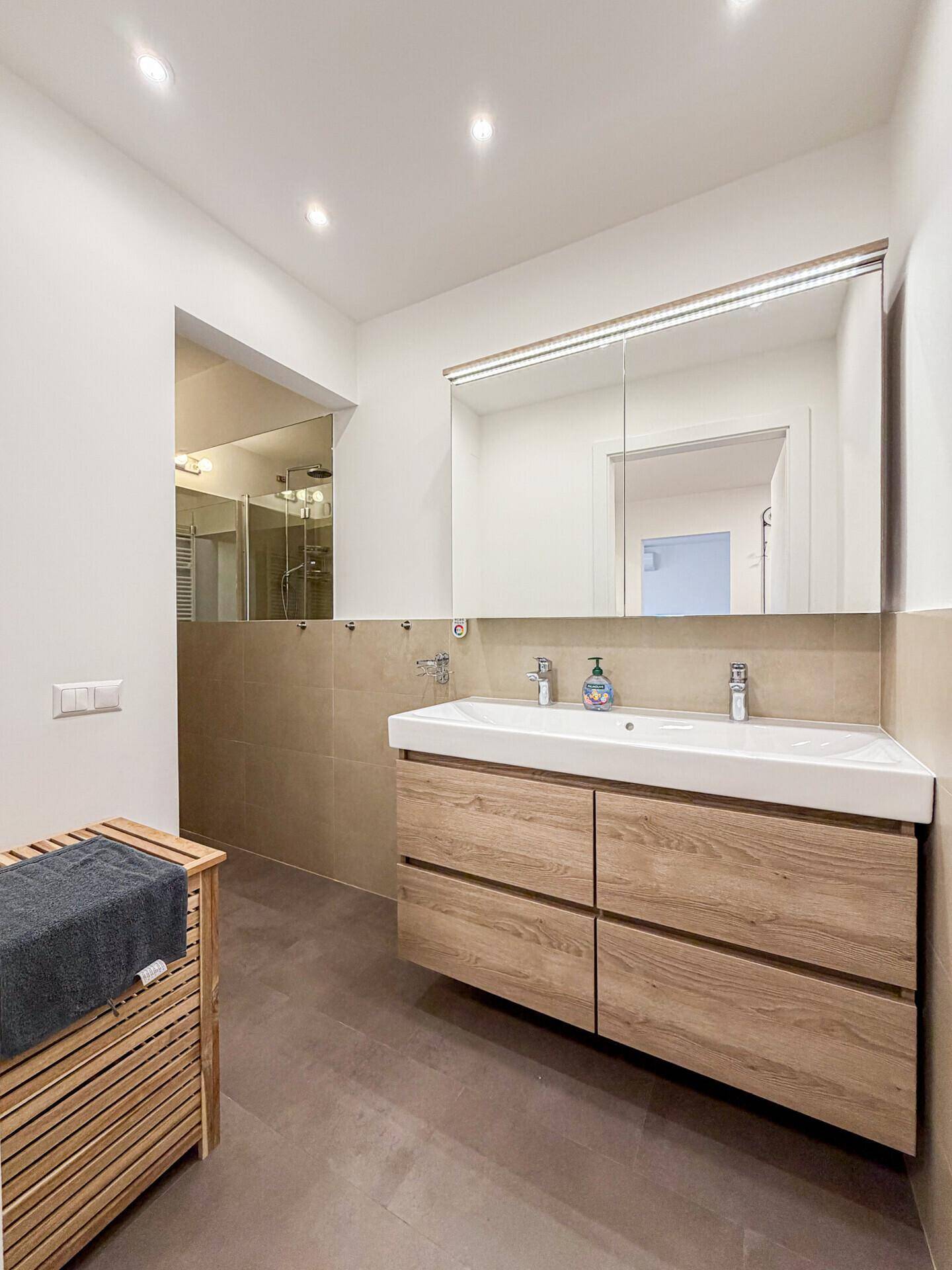 Geräumiges Badezimmer mit Doppelwaschbecken, Holzunterschrank und großem Spiegelschrank.