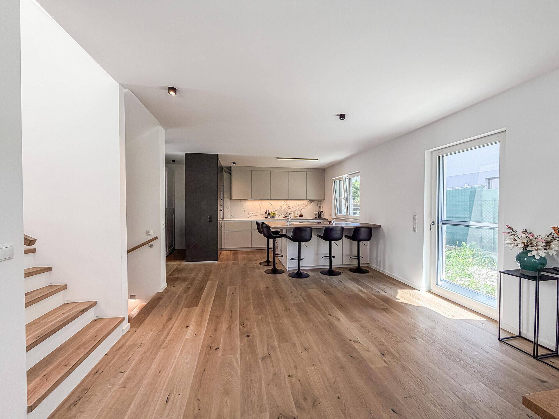 Heller offener Wohnbereich mit moderner Küche, Holzboden und Zugang zur Terrasse.