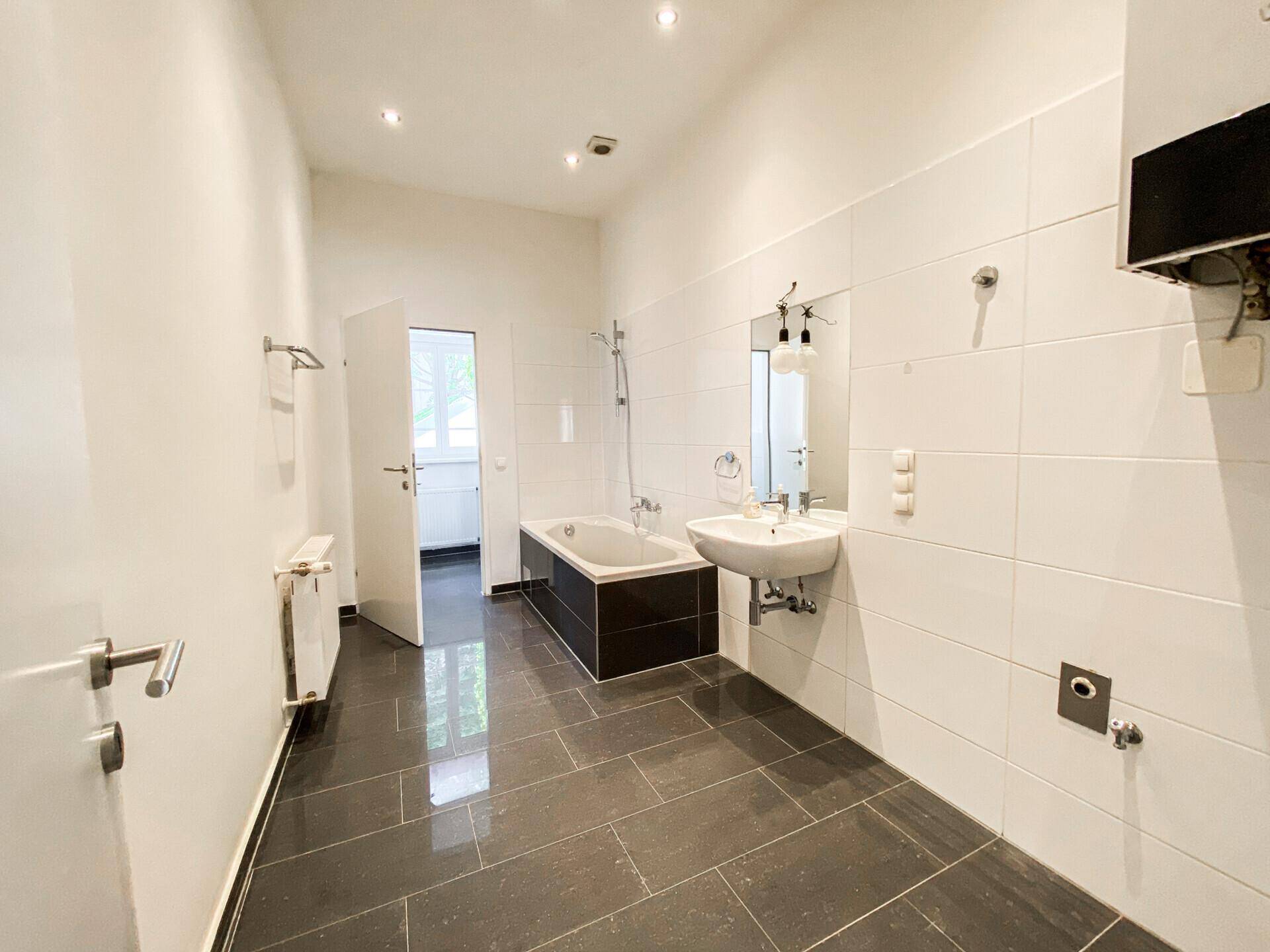 Geräumiges Badezimmer mit dunklen Fliesen, Badewanne und Waschbecken.