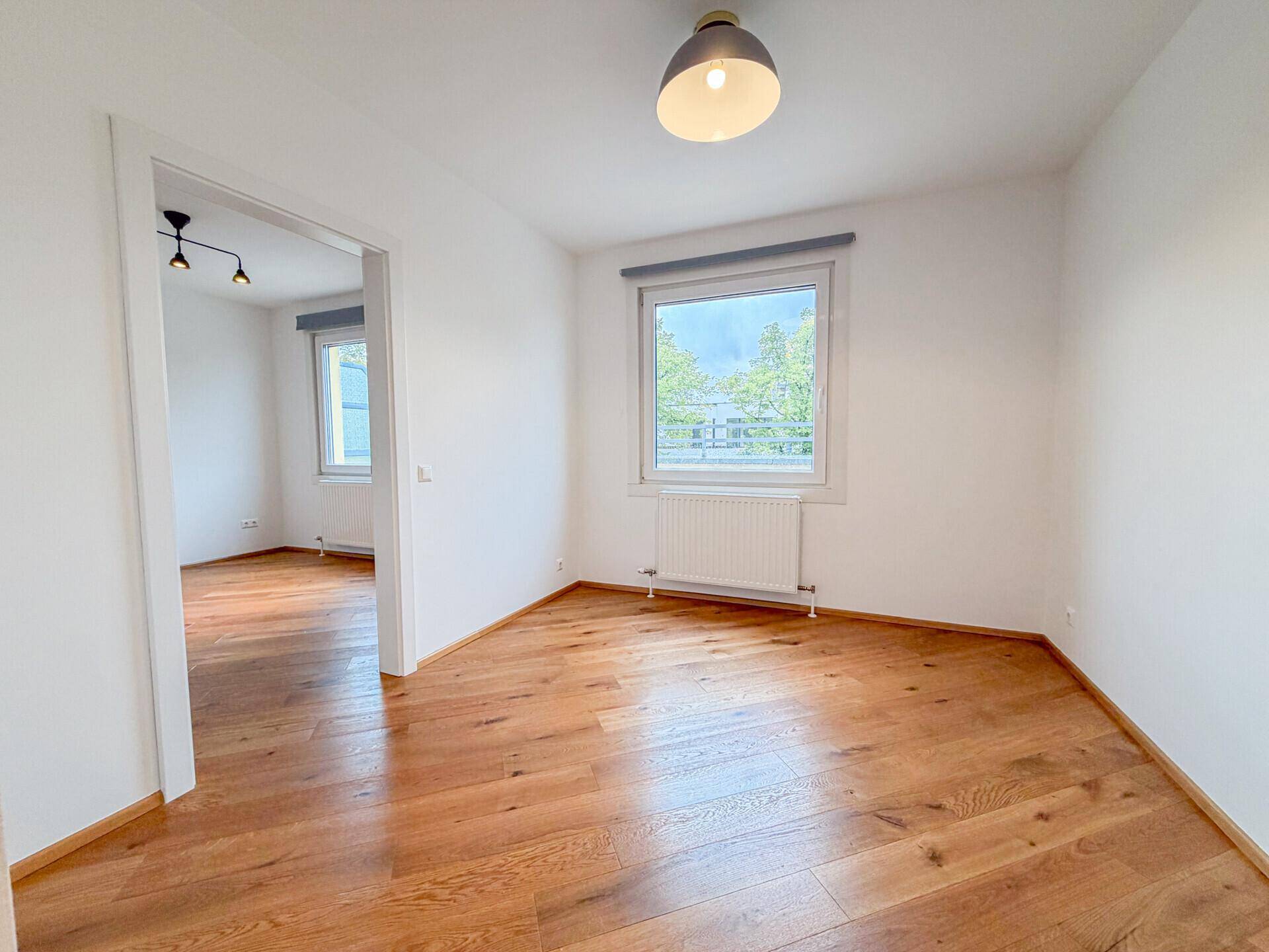 Helles Zimmer mit Holzboden und Blick ins Grüne, ideal als Schlaf- oder Arbeitszimmer.