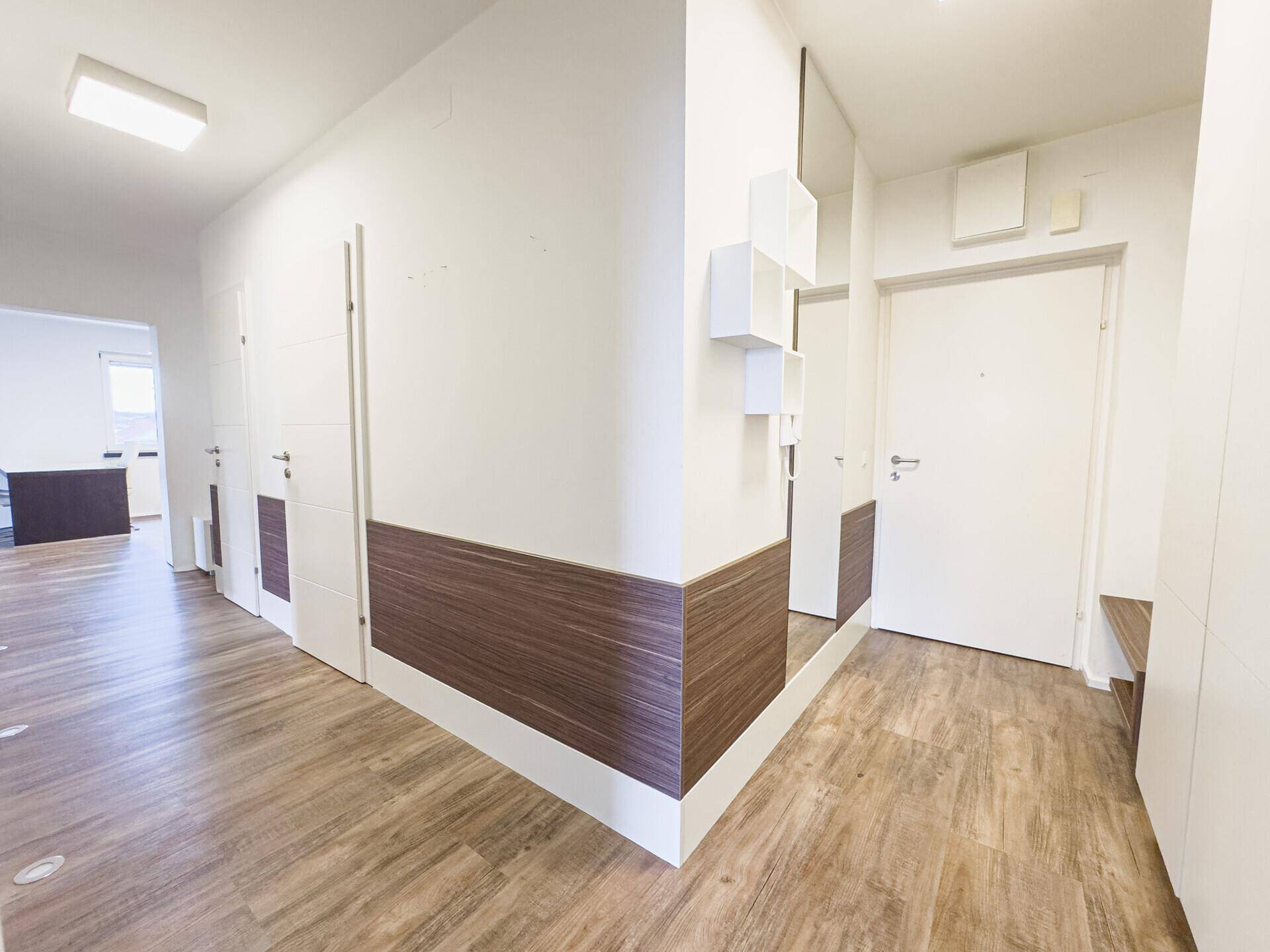 Heller Flur mit Laminatboden und modernen Wandverkleidungen, führt zu weiteren Räumen.
